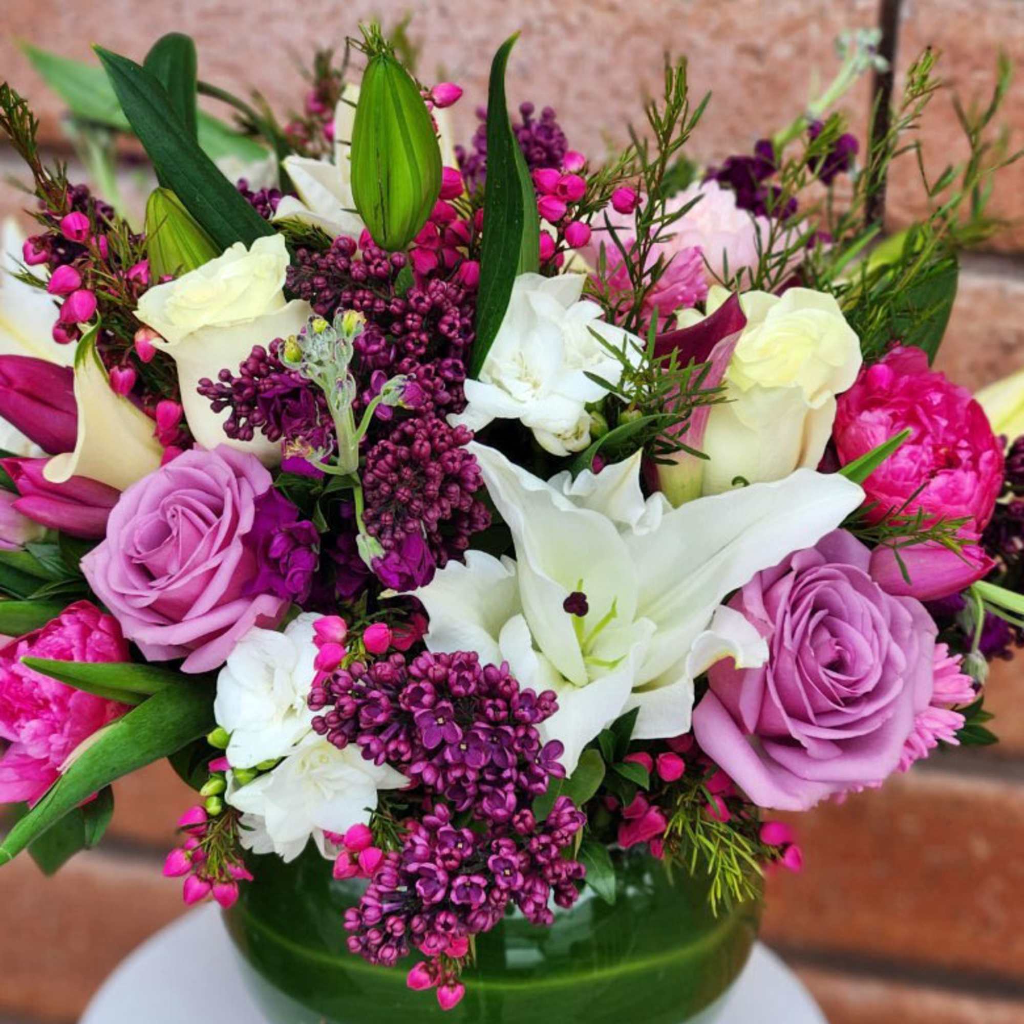 Mixed bouquet of purple roses, white lilies, and pink blooms in a clear glass vase