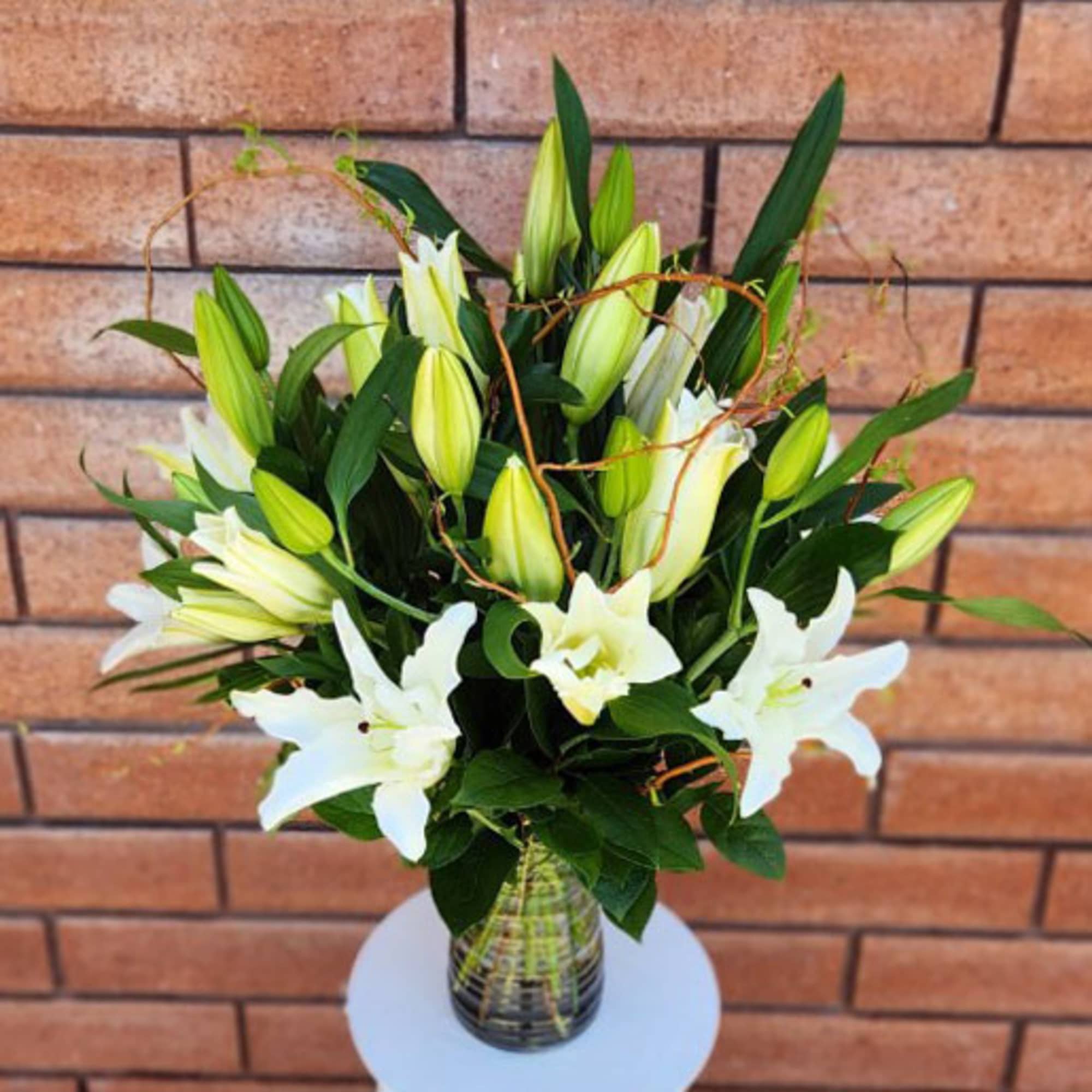 Tall arrangement of white lilies and buds in a clear glass vase