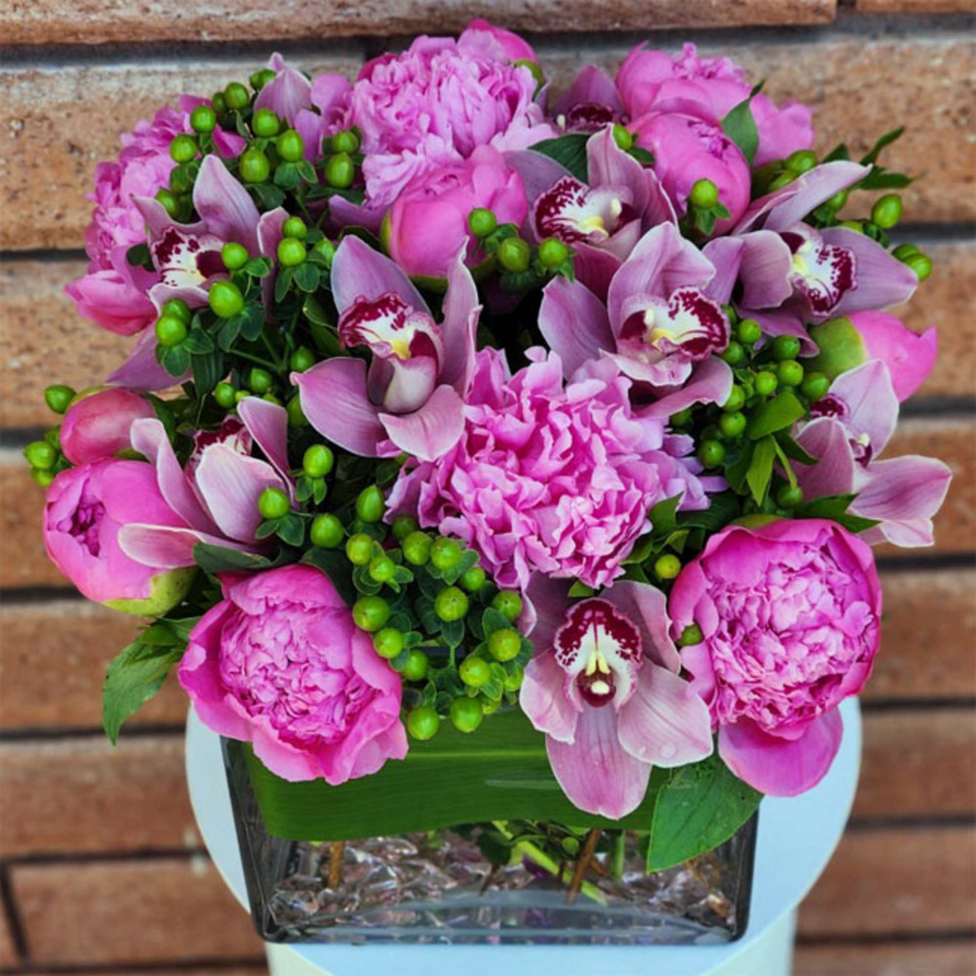 Pink peonies and orchids arranged in a glass vase