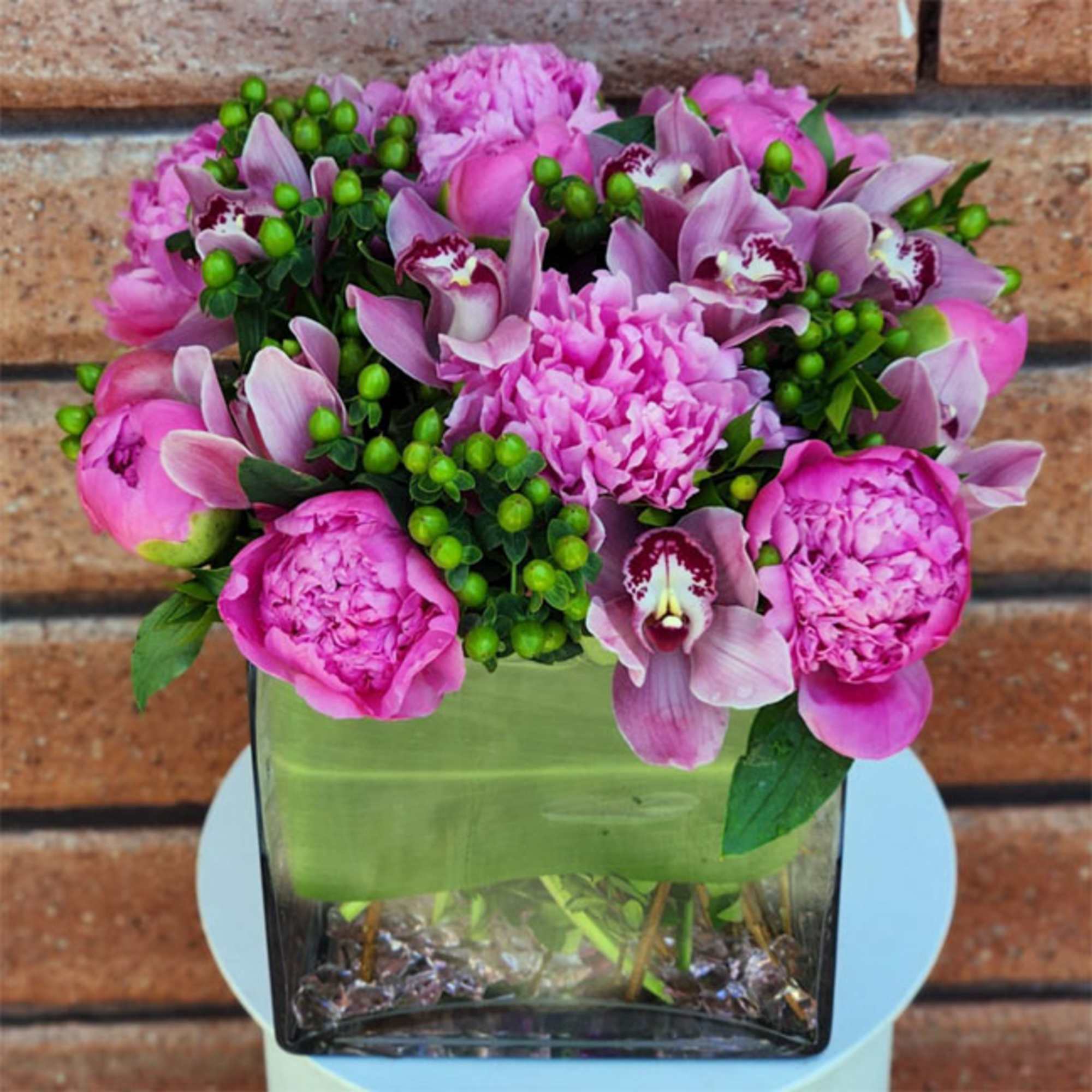 Pink peonies and orchids arranged in a square glass vase