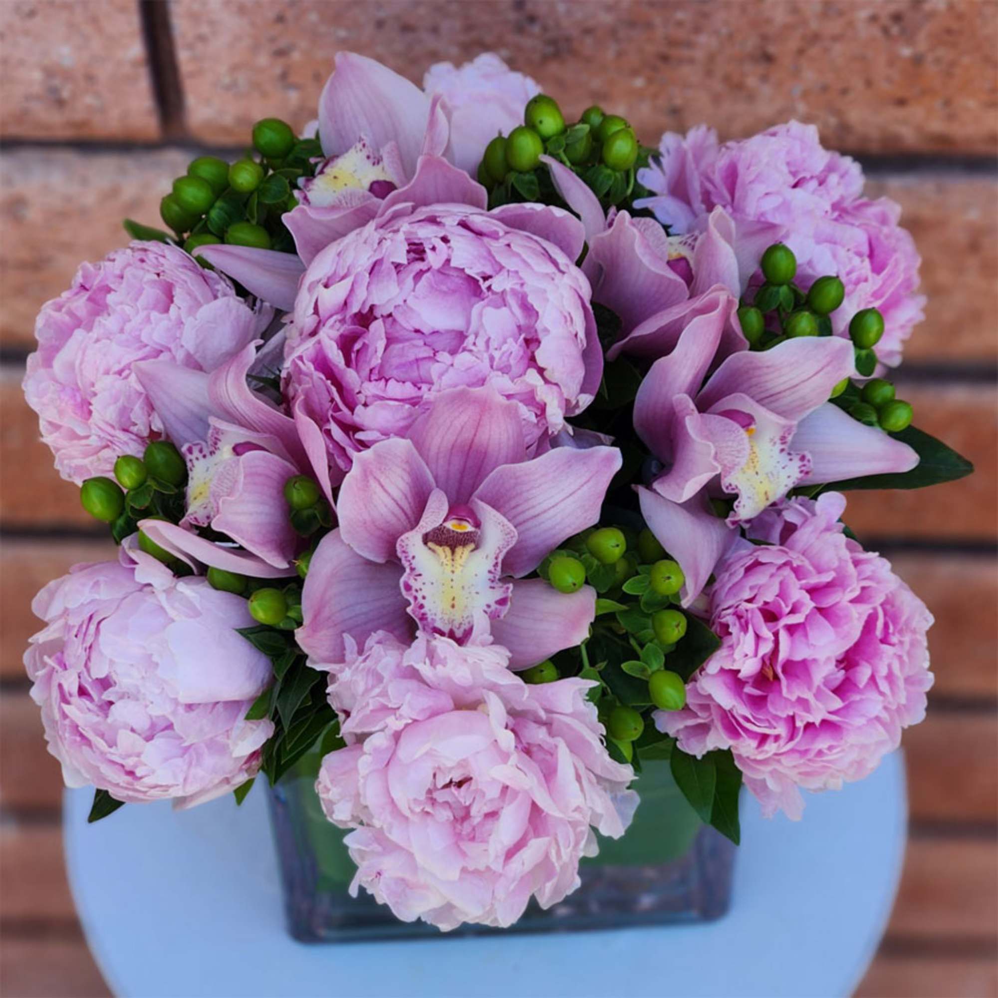 Pink peonies and orchids arranged in a square glass vase