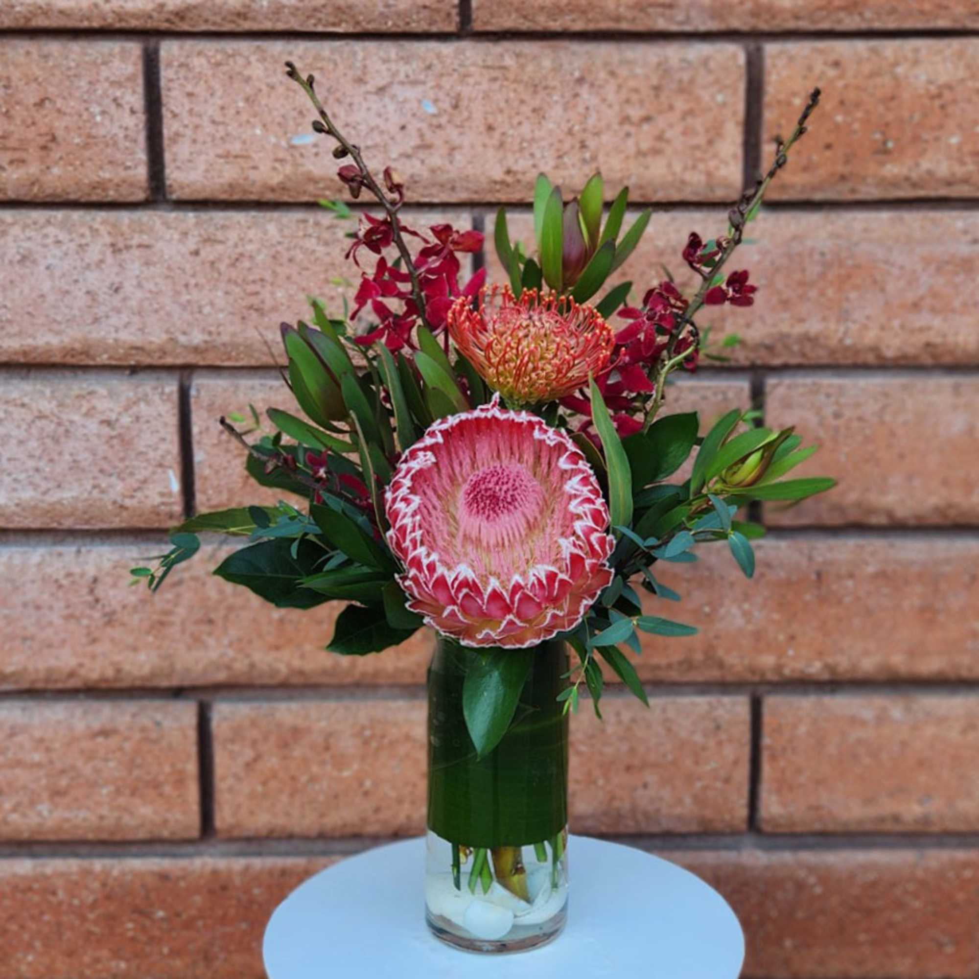 Pink protea arrangement in a glass vase with red orchid accents