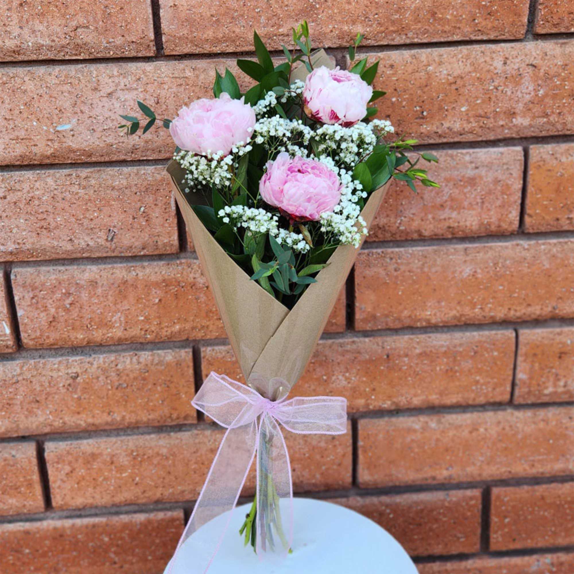 Pink peony bouquet wrapped in brown paper with a pink ribbon