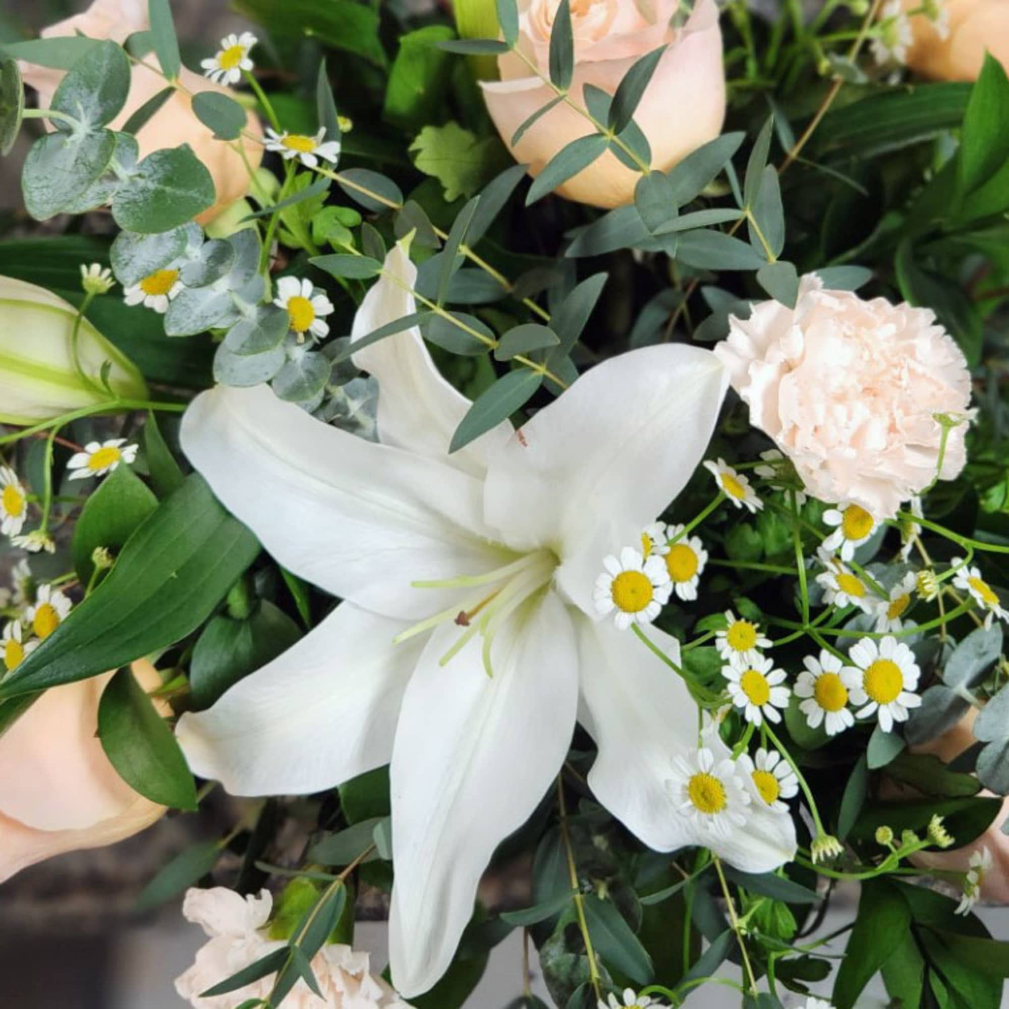 Arrangement with a white lily, peach roses, carnations, and small white daisies.