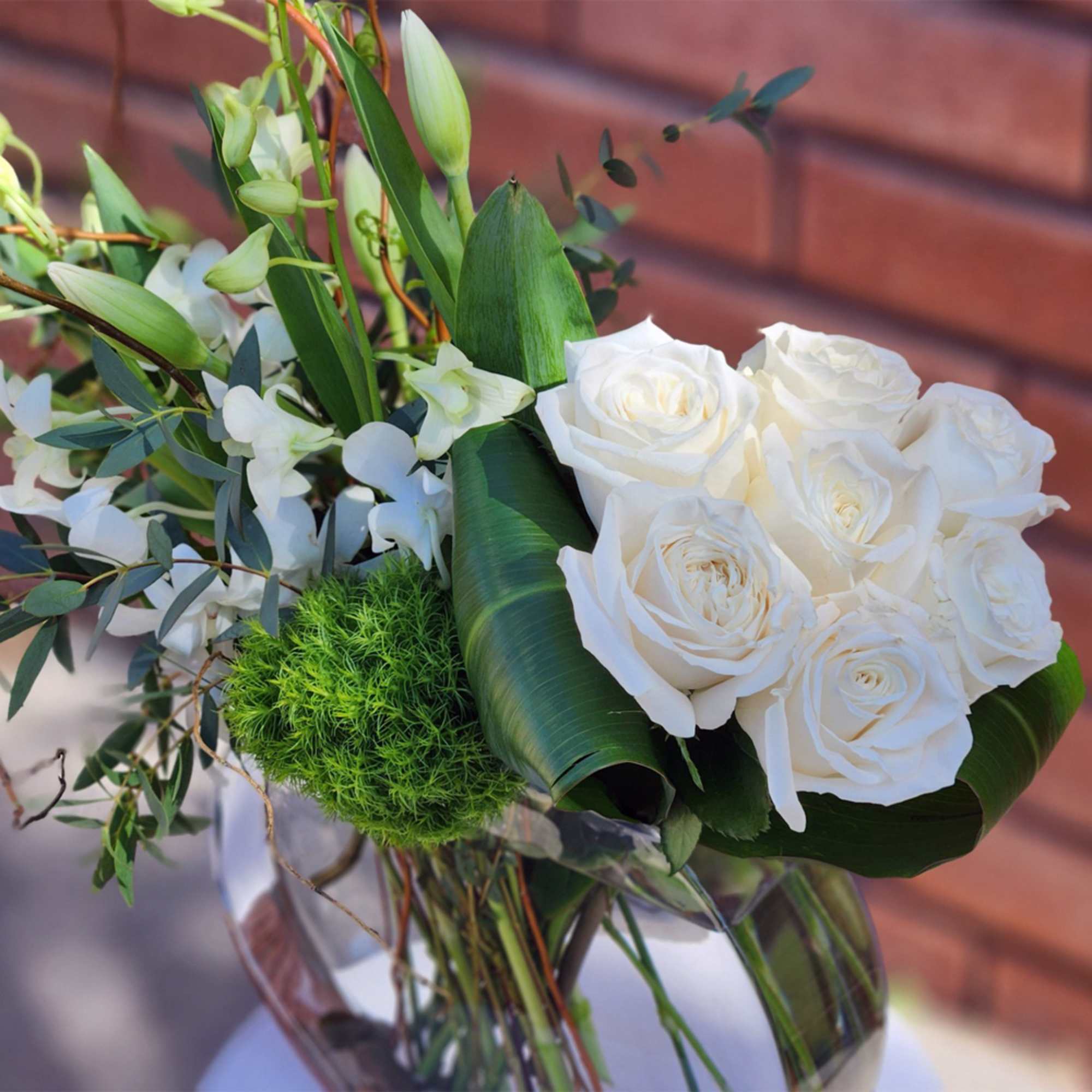 White roses and orchids arranged in a glass vase