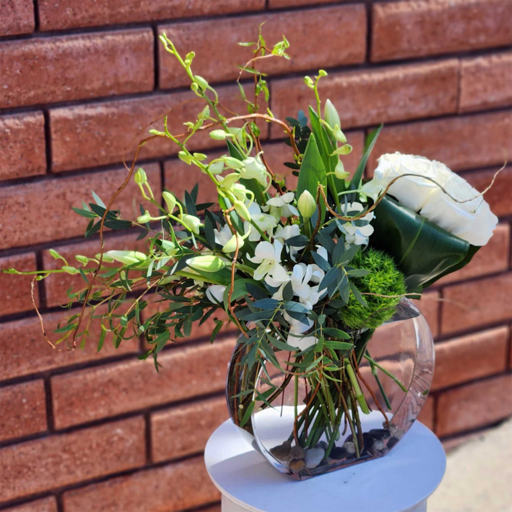 White floral arrangement in a clear glass vase with green accents