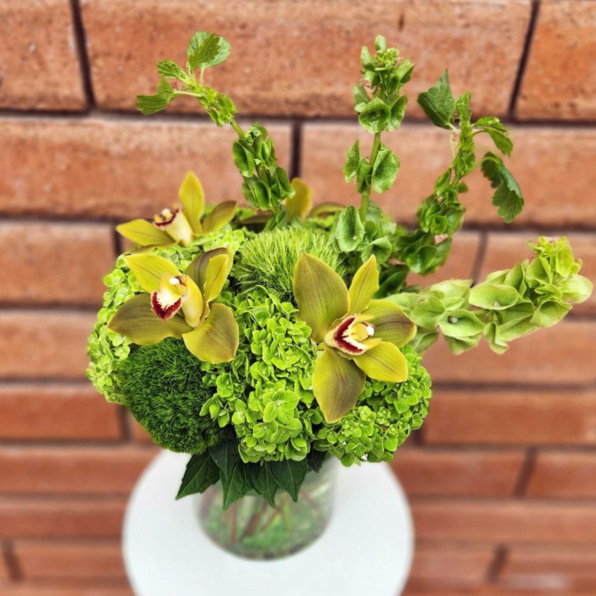 Green floral arrangement with yellow orchids in a glass vase