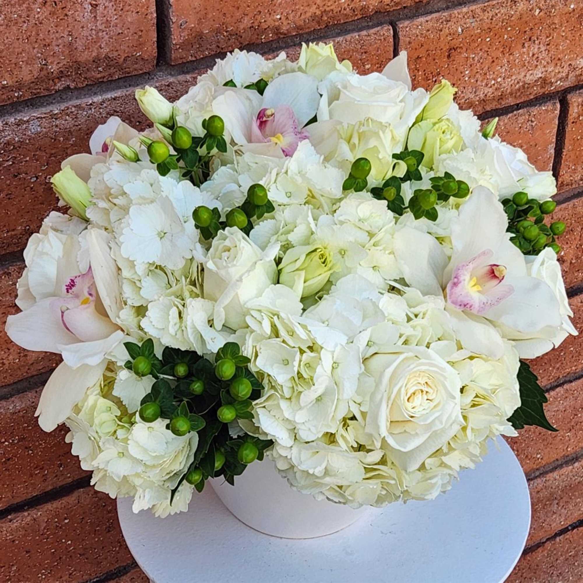 White floral arrangement in a round white box with pale pink orchids