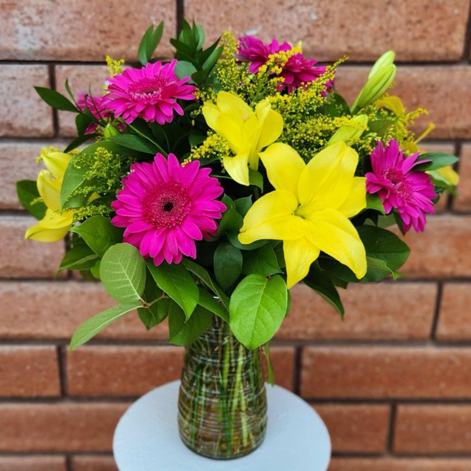 Pink gerbera daisies and yellow lilies in a glass vase