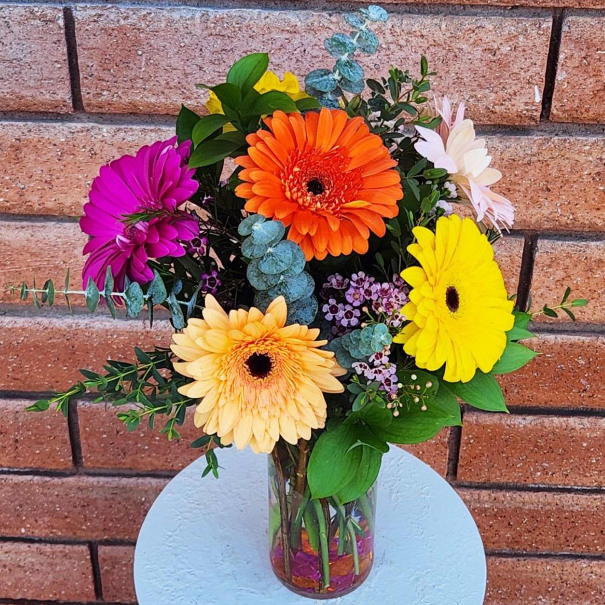 Bright mixed gerbera daisy arrangement in a clear glass vase with colorful filler flowers.