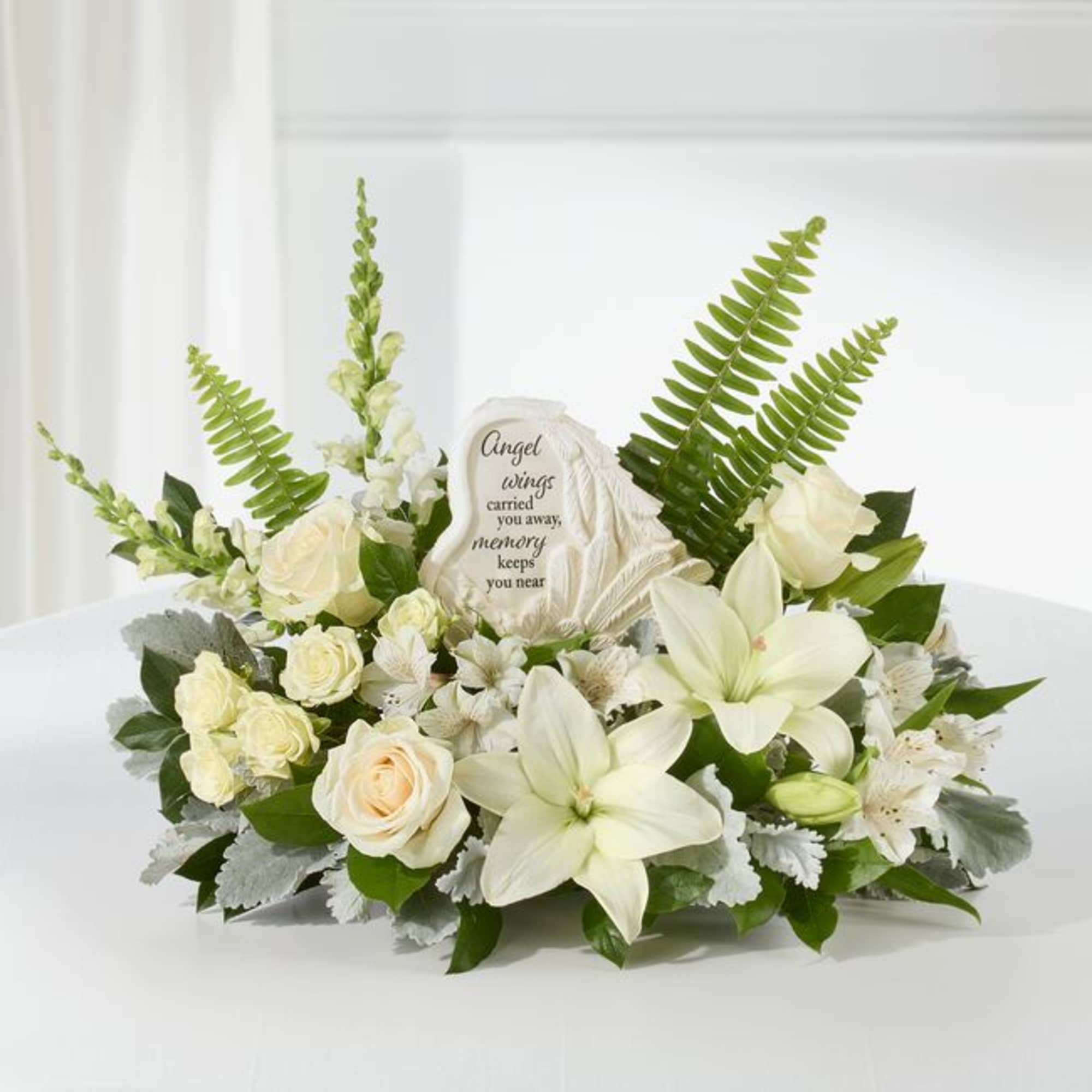 White floral sympathy arrangement with roses, lilies, and a memorial plaque