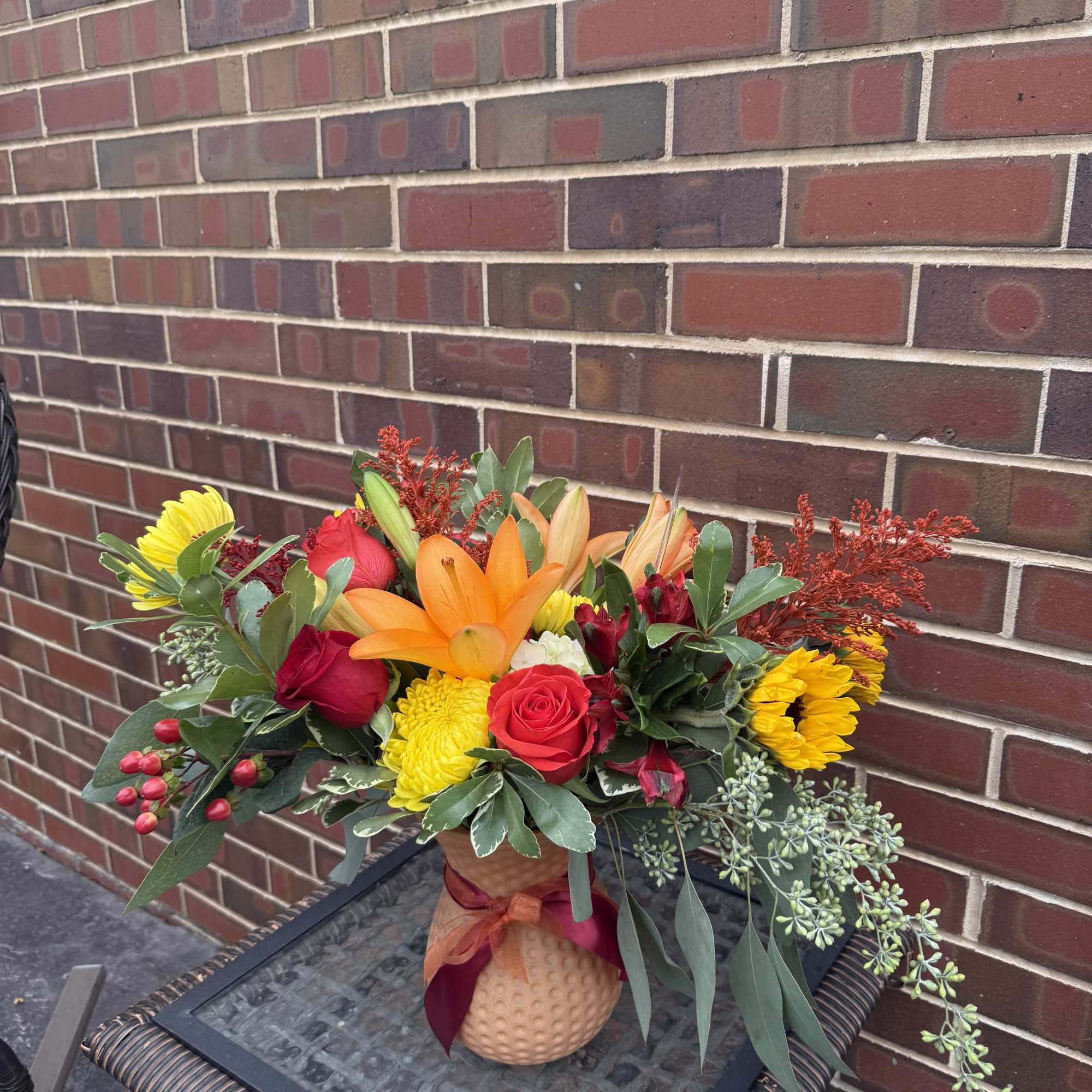 Mixed bouquet in a textured vase with red, yellow, and orange flowers