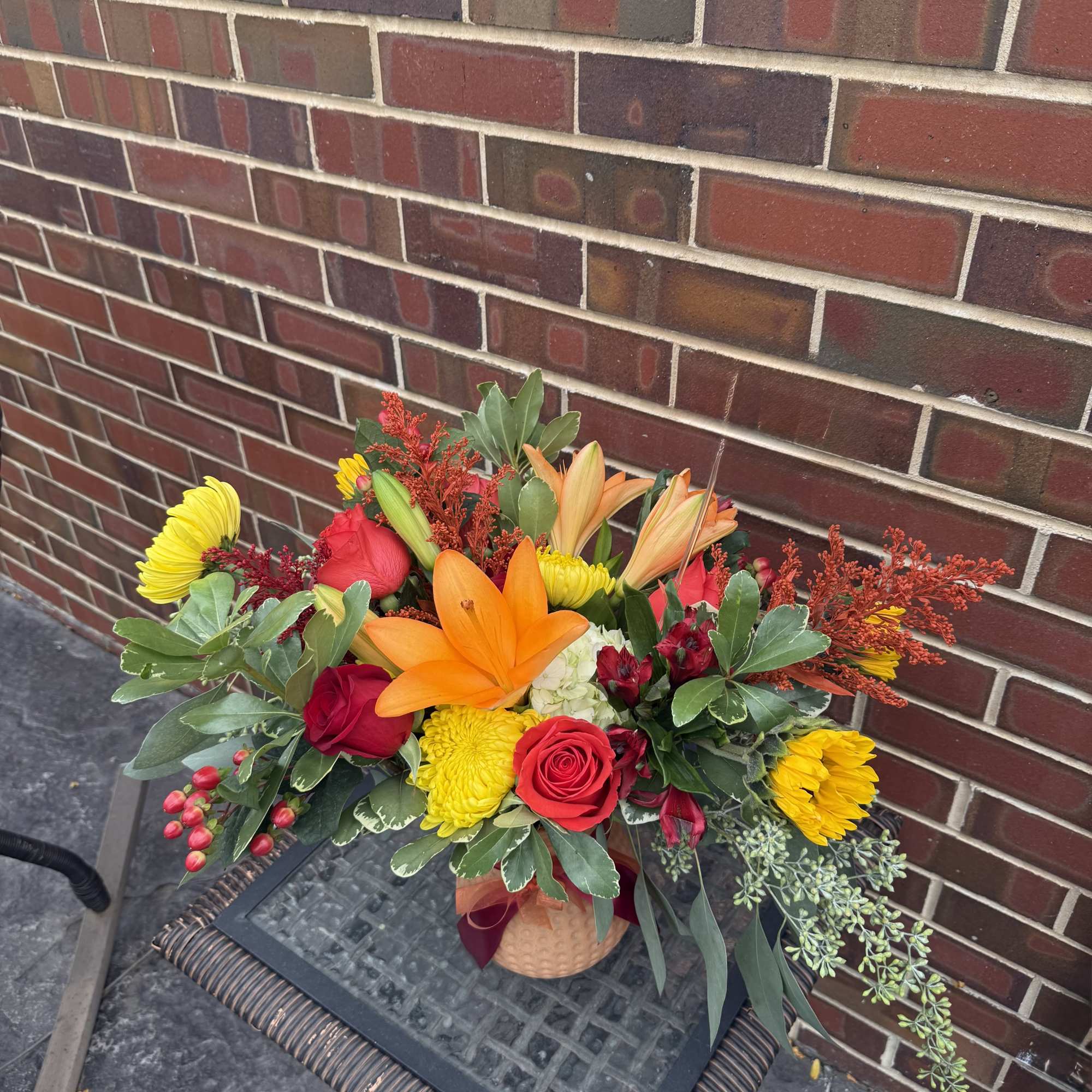Bright mixed bouquet in a woven basket with orange lilies and red roses
