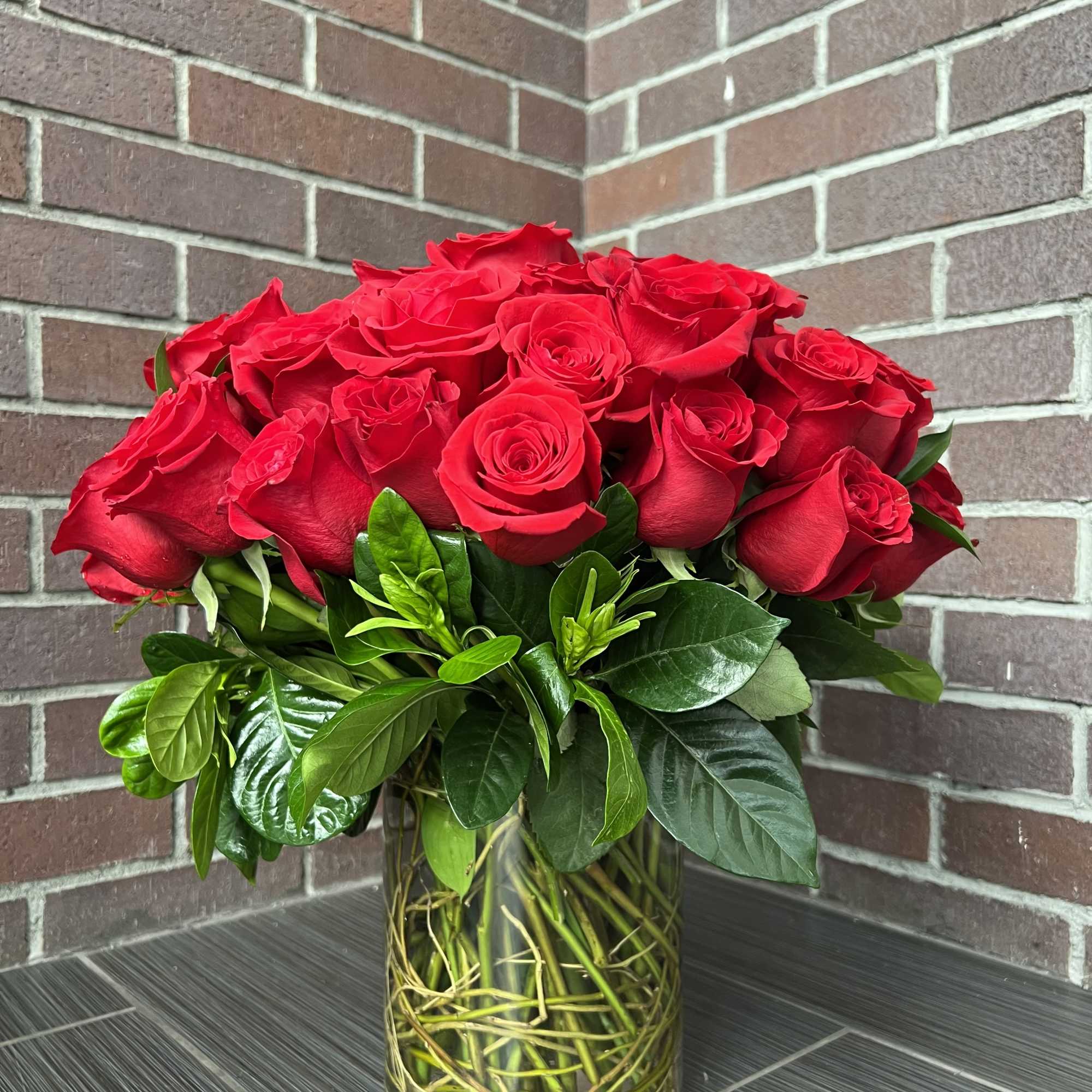 Red roses arranged in a clear glass vase with glossy greenery