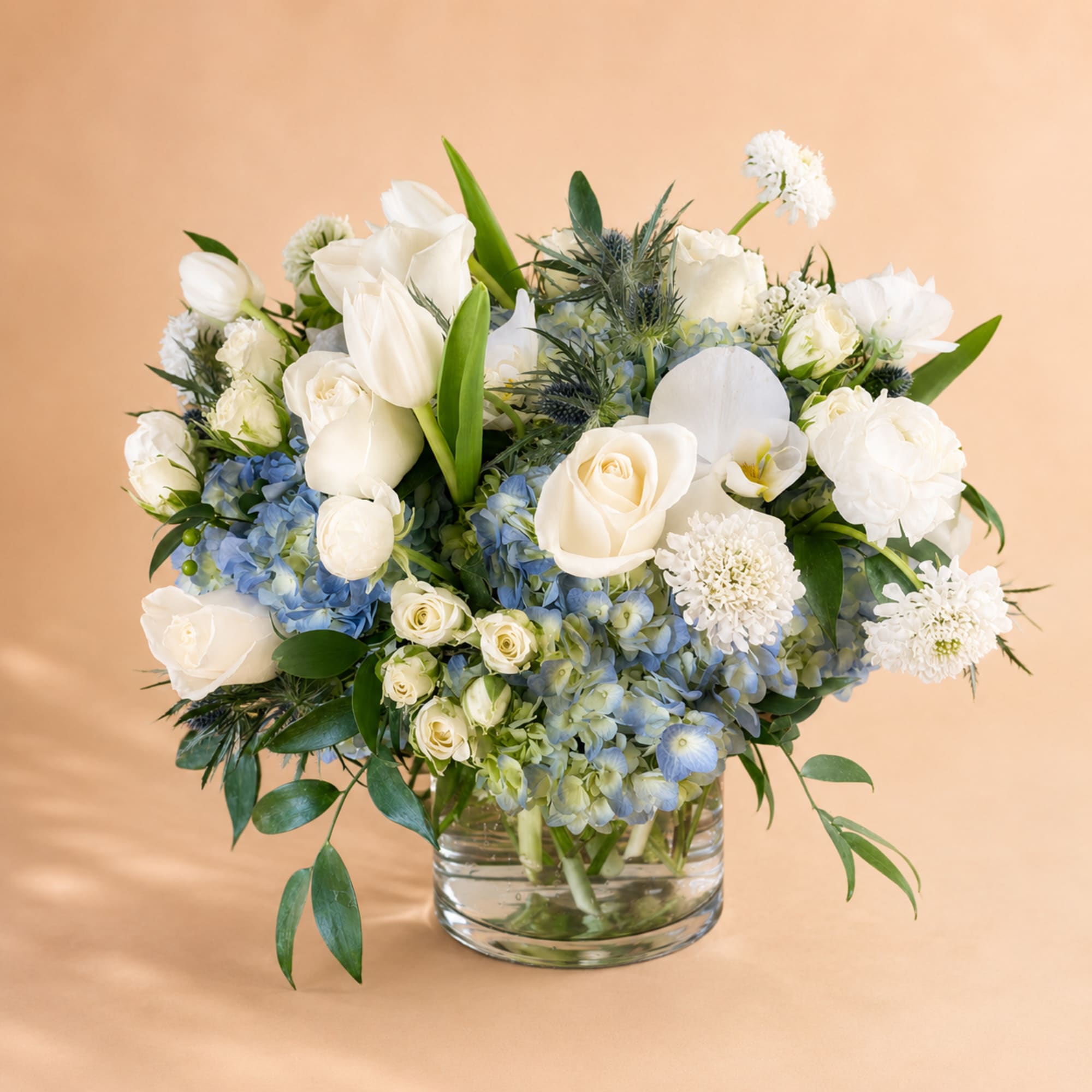 White roses and tulips with blue hydrangeas in a glass vase
