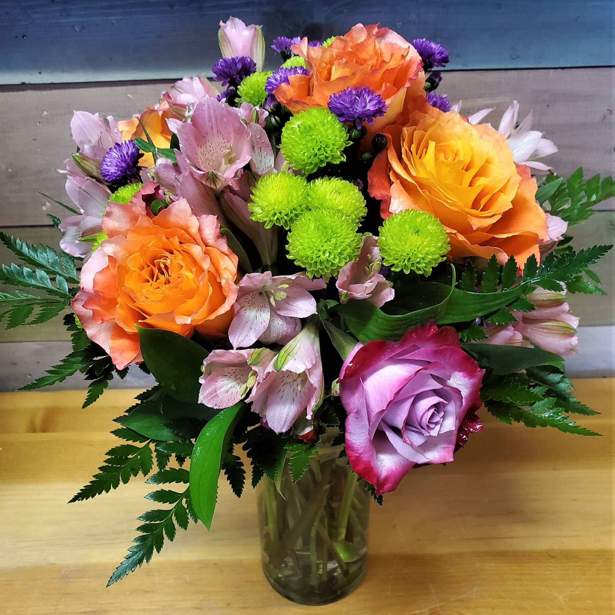 Mixed bouquet of orange and lavender roses with pink alstroemeria in a glass vase