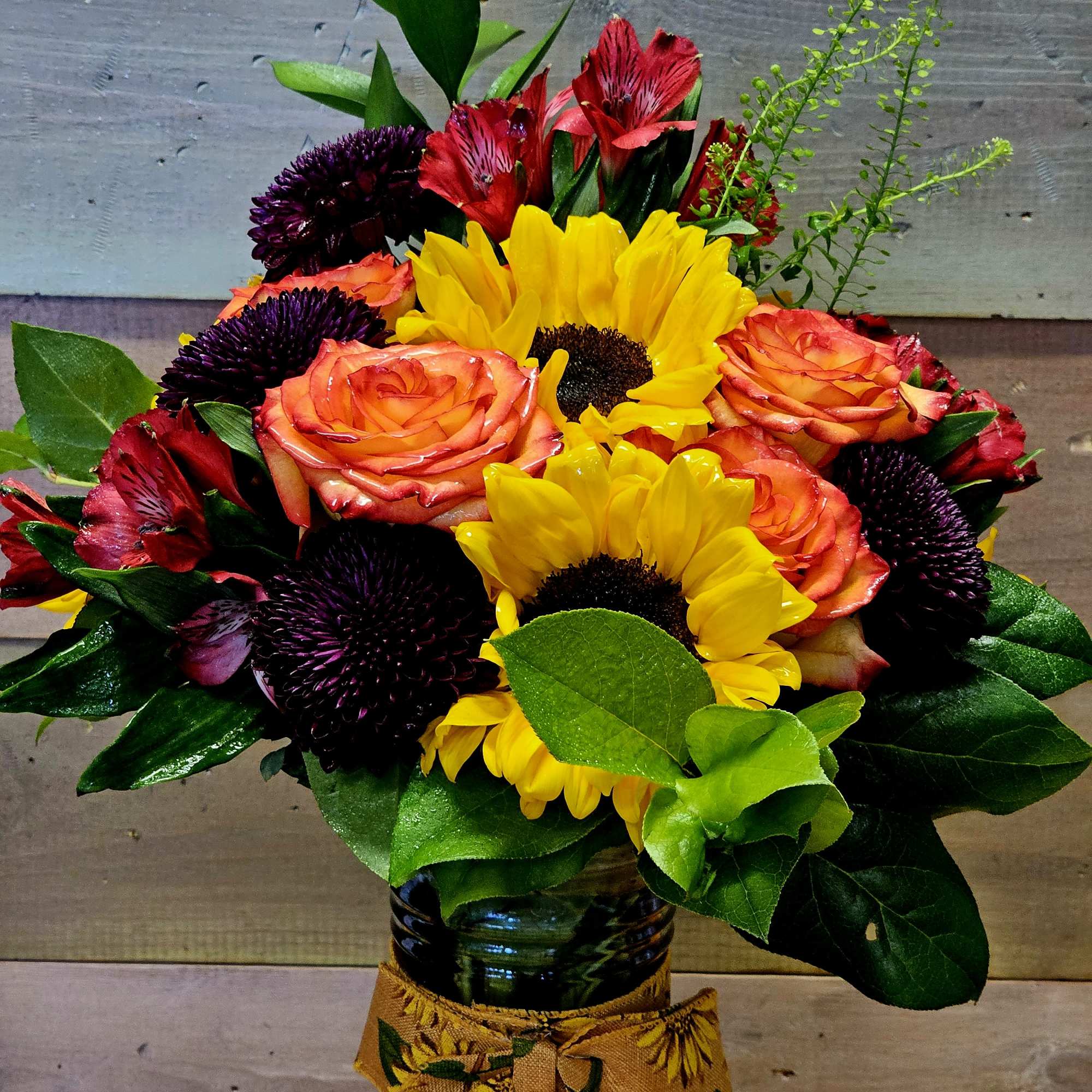 Mixed bouquet of sunflowers, orange roses, and red alstroemeria in a glass vase