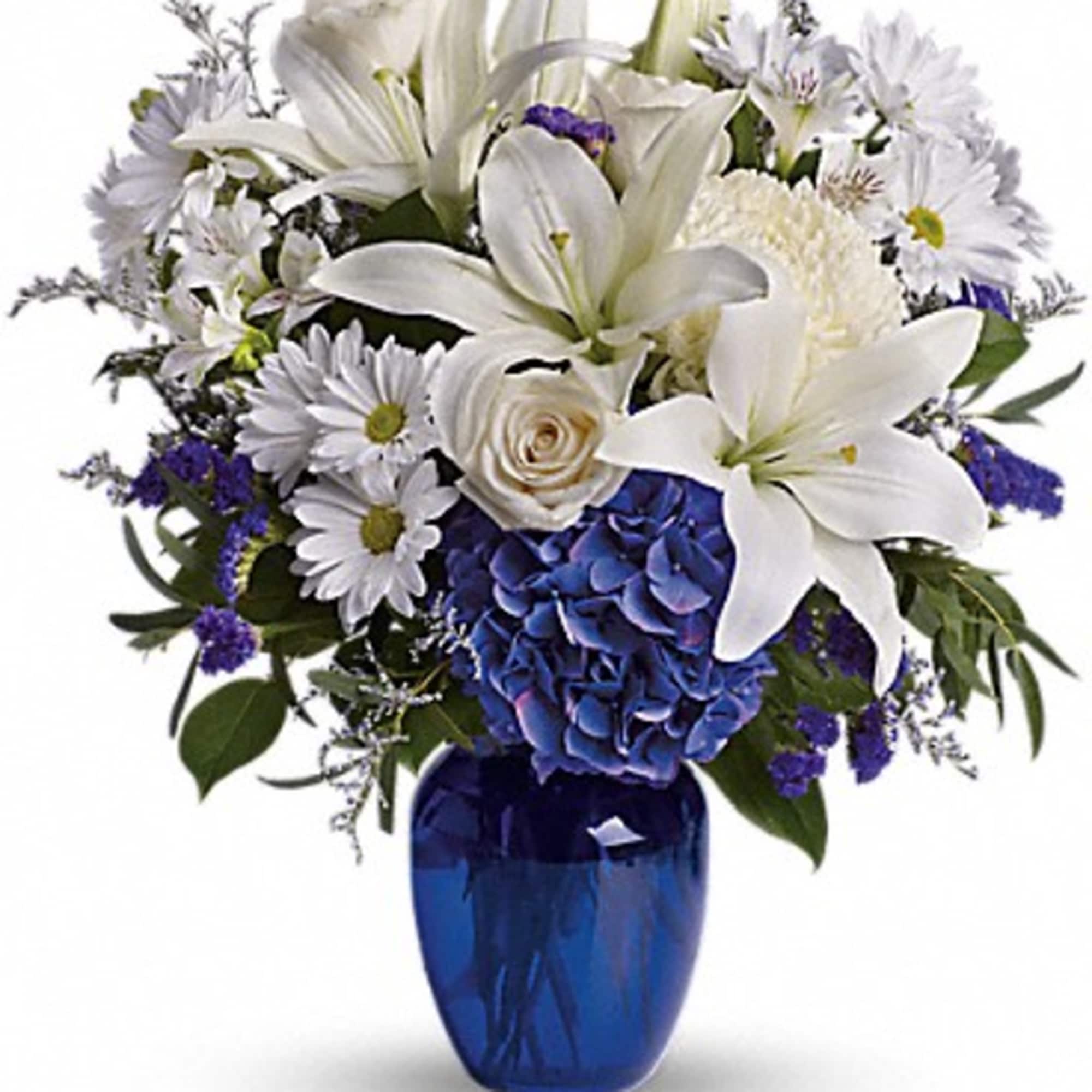 White lilies and daisies arranged in a blue glass vase