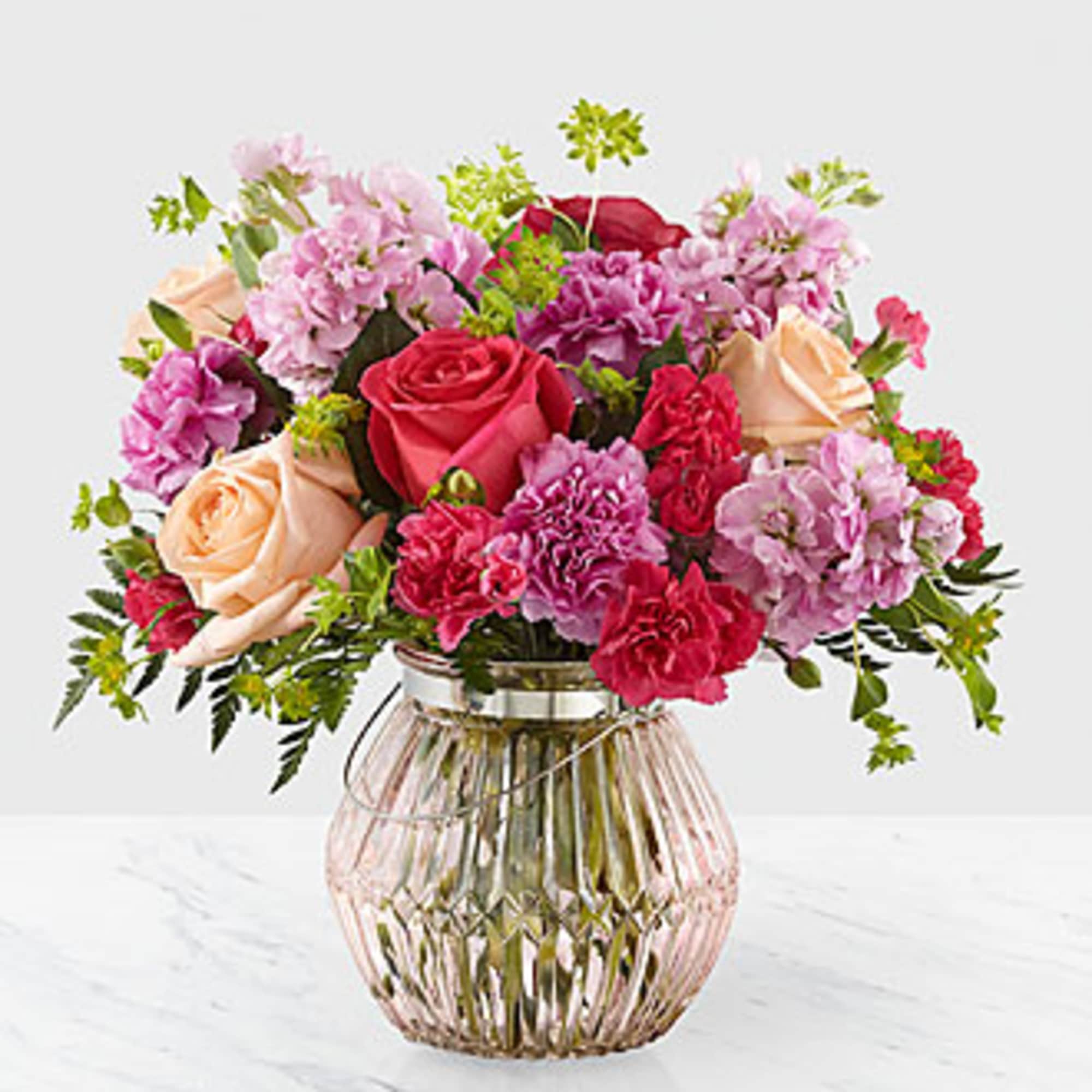 Pink and peach roses with purple carnations in a glass vase