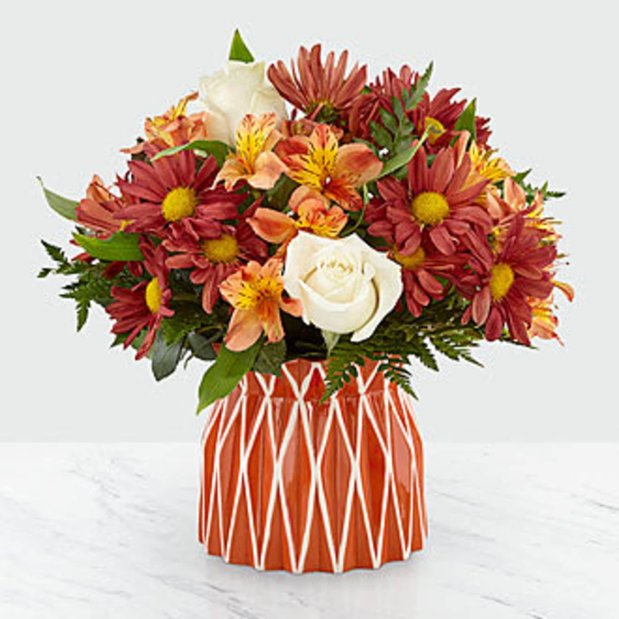 Bouquet of red daisies, white roses, and orange alstroemeria in a patterned vase