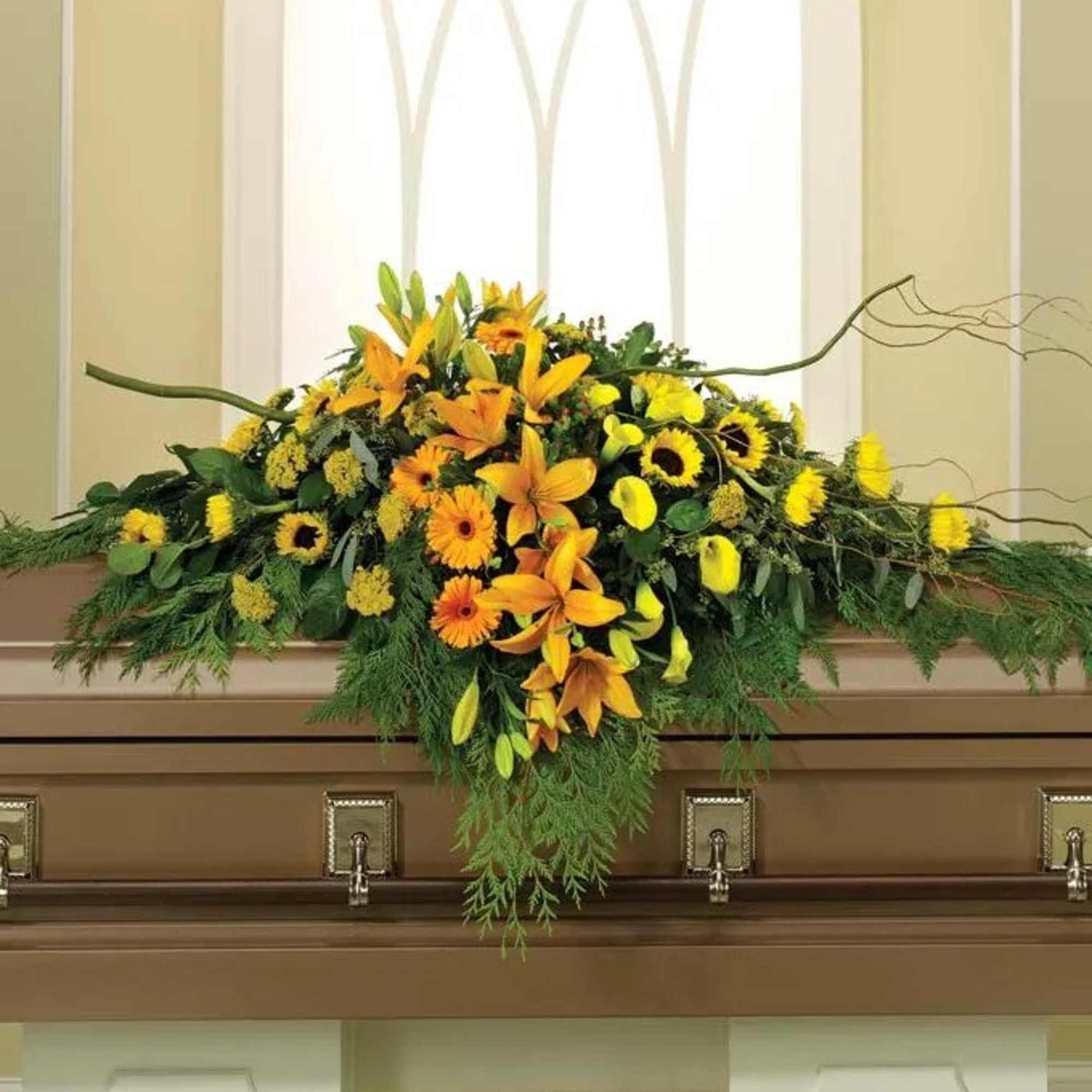 Yellow and orange floral casket spray with trailing greenery