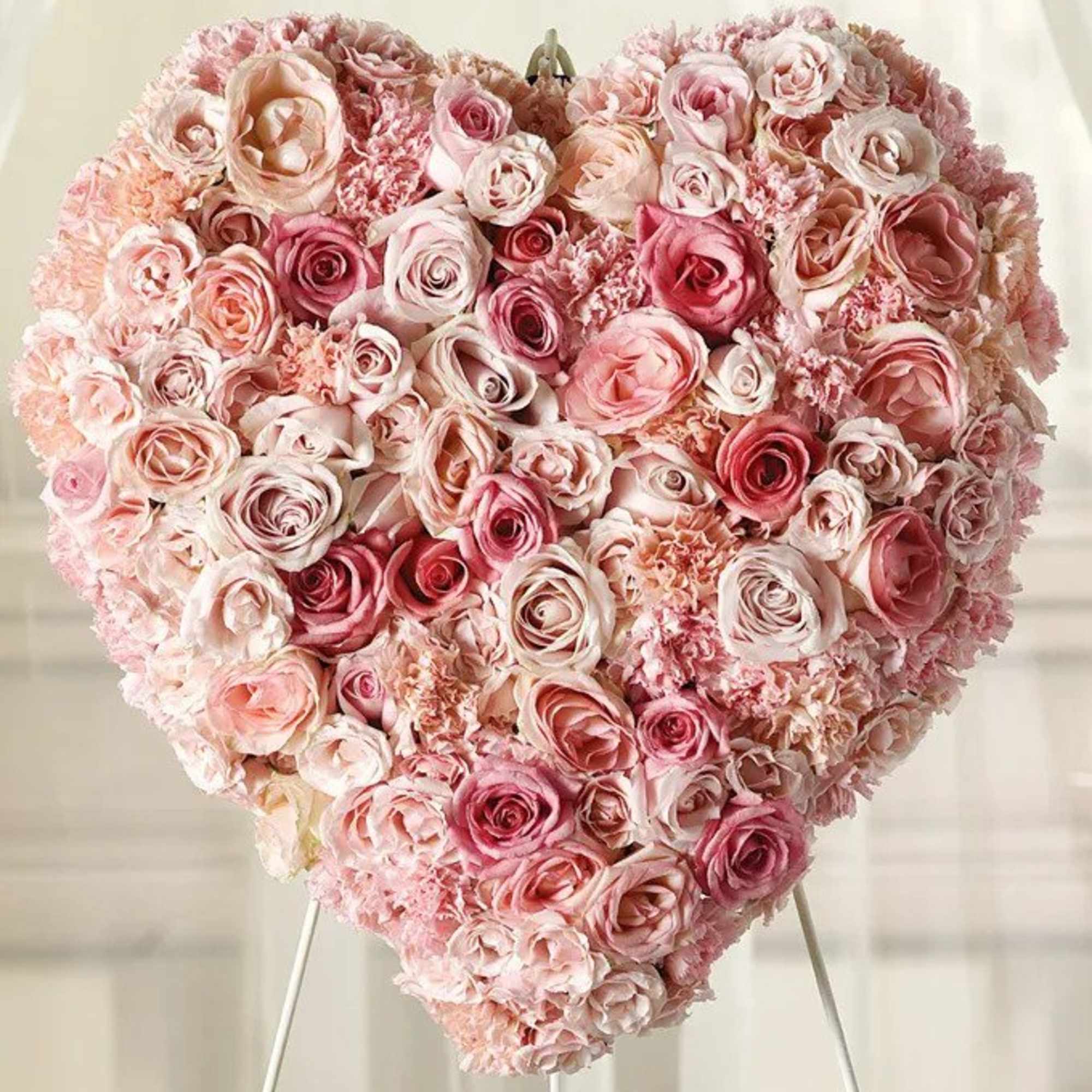 Delicate pink roses and carnations fill this heart shaped arrangement for a