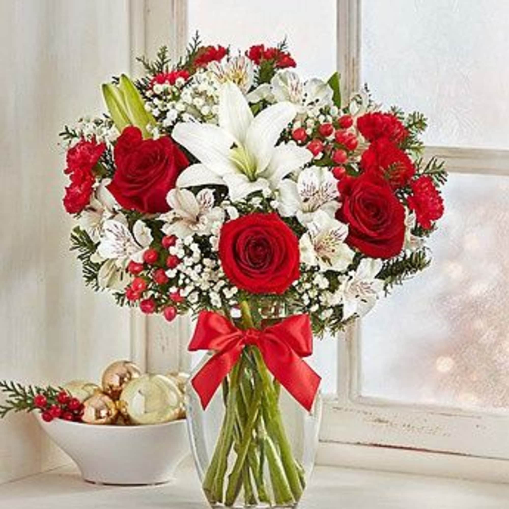 Red roses and white lilies in a clear glass vase with a red bow