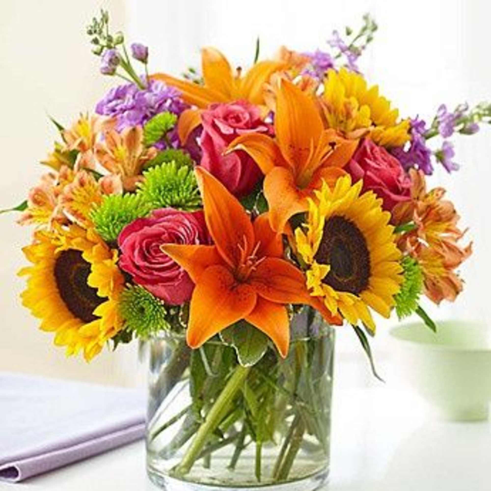 Bouquet of sunflowers, orange lilies, and pink roses in a glass vase