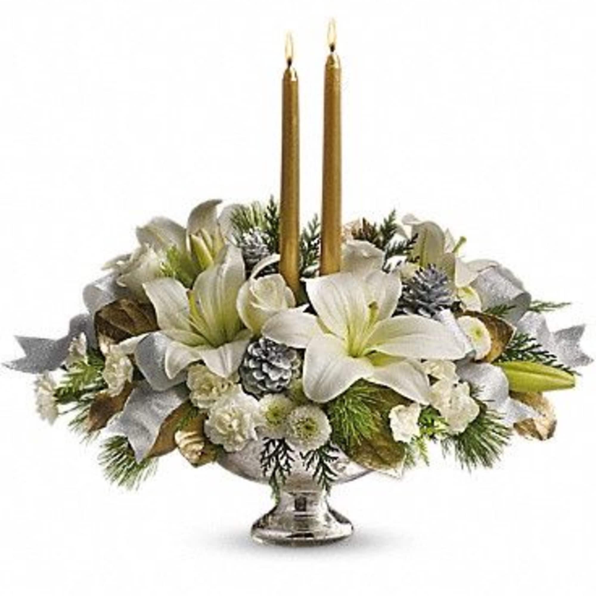 White lilies arranged around two gold taper candles in a silver pedestal bowl
