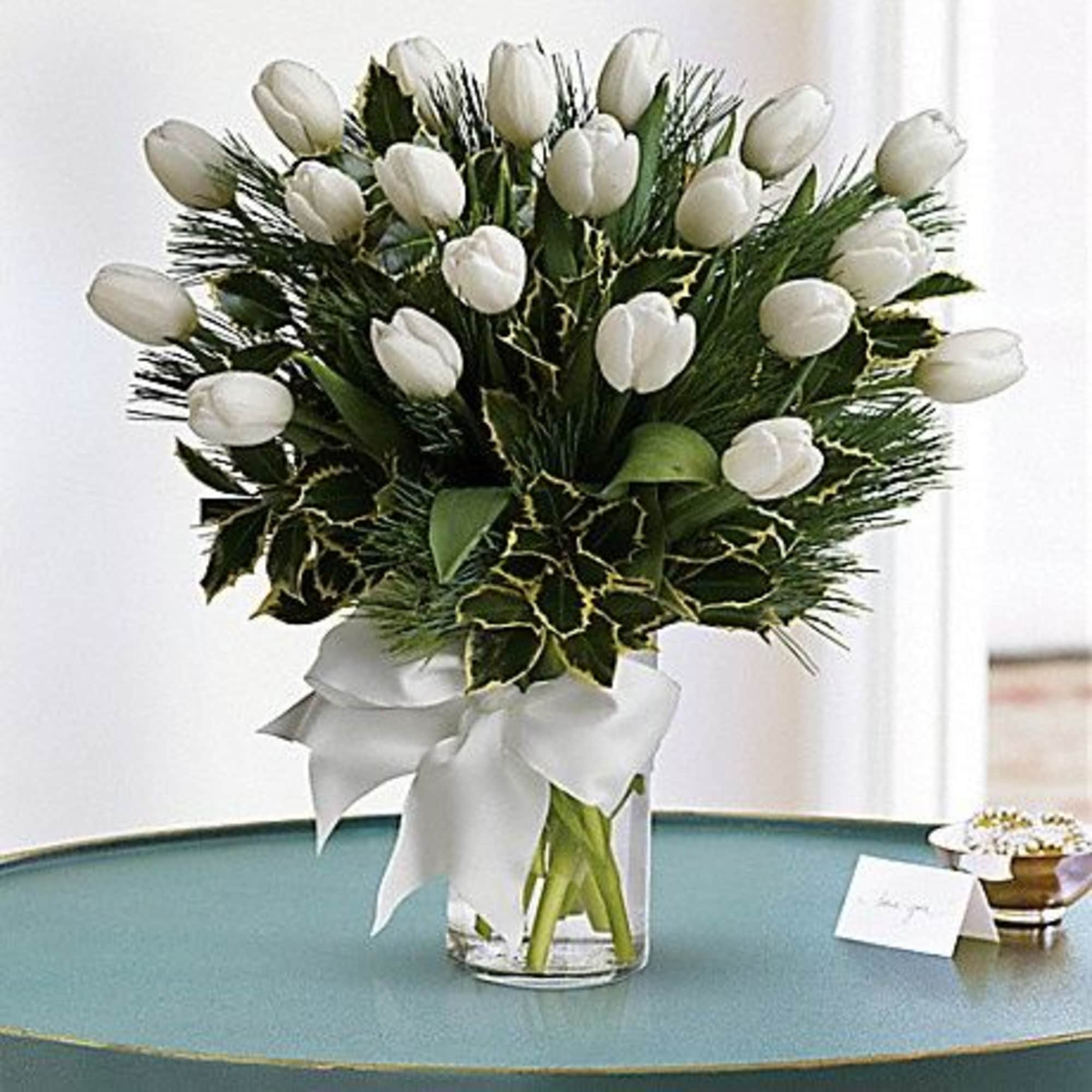 White tulips arranged in a clear glass vase with a white ribbon