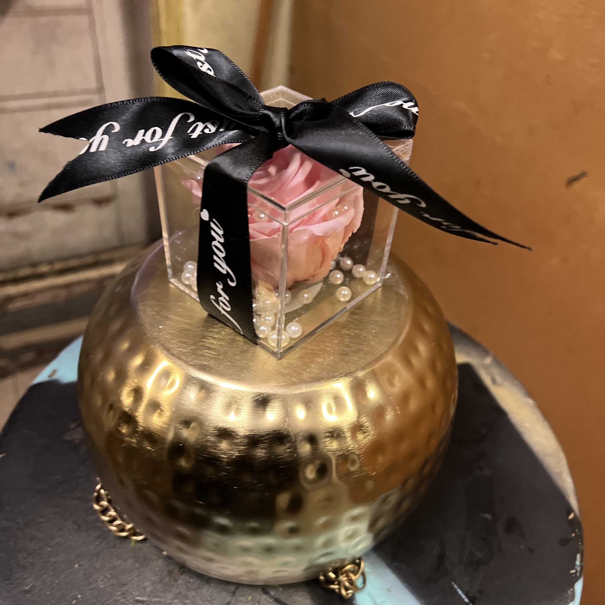 Pink rose in a clear gift box atop a gold vase