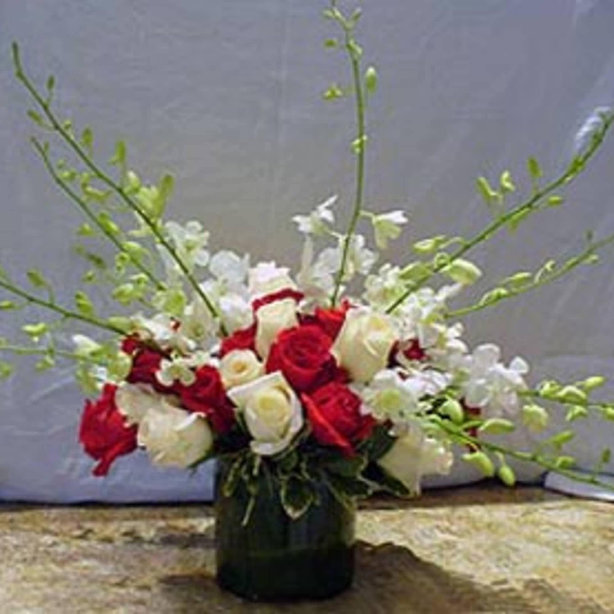 Red and white rose arrangement with white orchids and green sprays in a glass cylinder vase