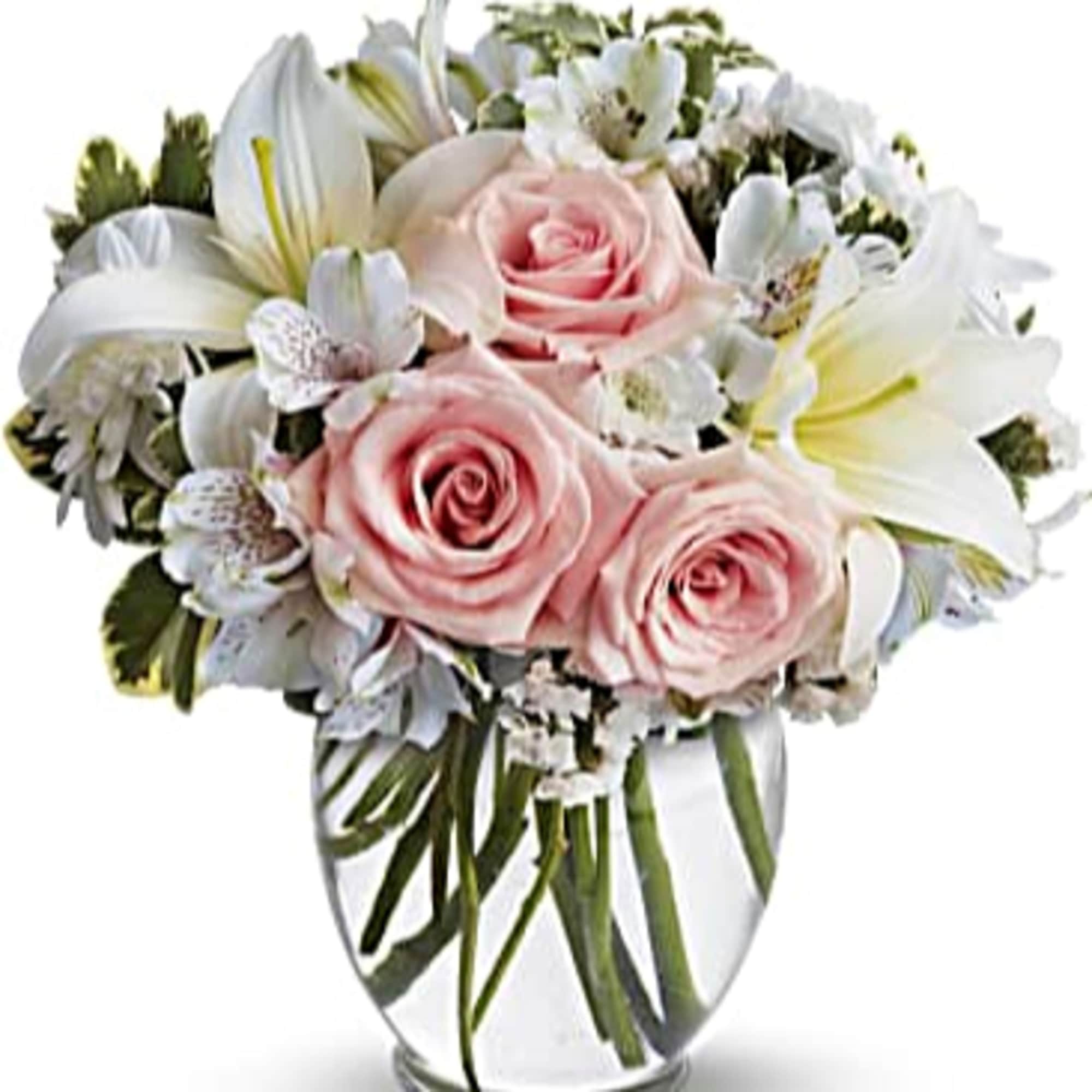 Round glass vase arrangement with pale pink roses, white lilies, and white accent flowers.