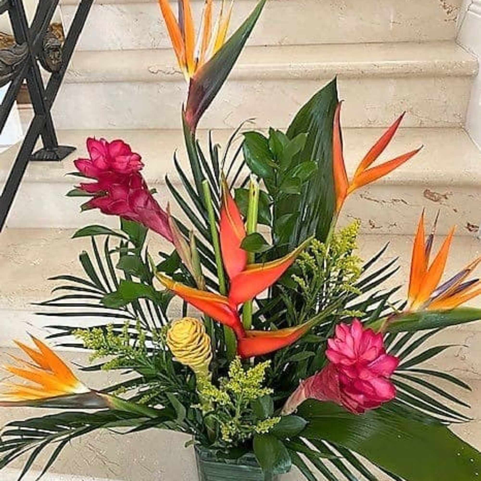 Tall tropical arrangement with orange and pink flowers and lush foliage in a low rectangular container