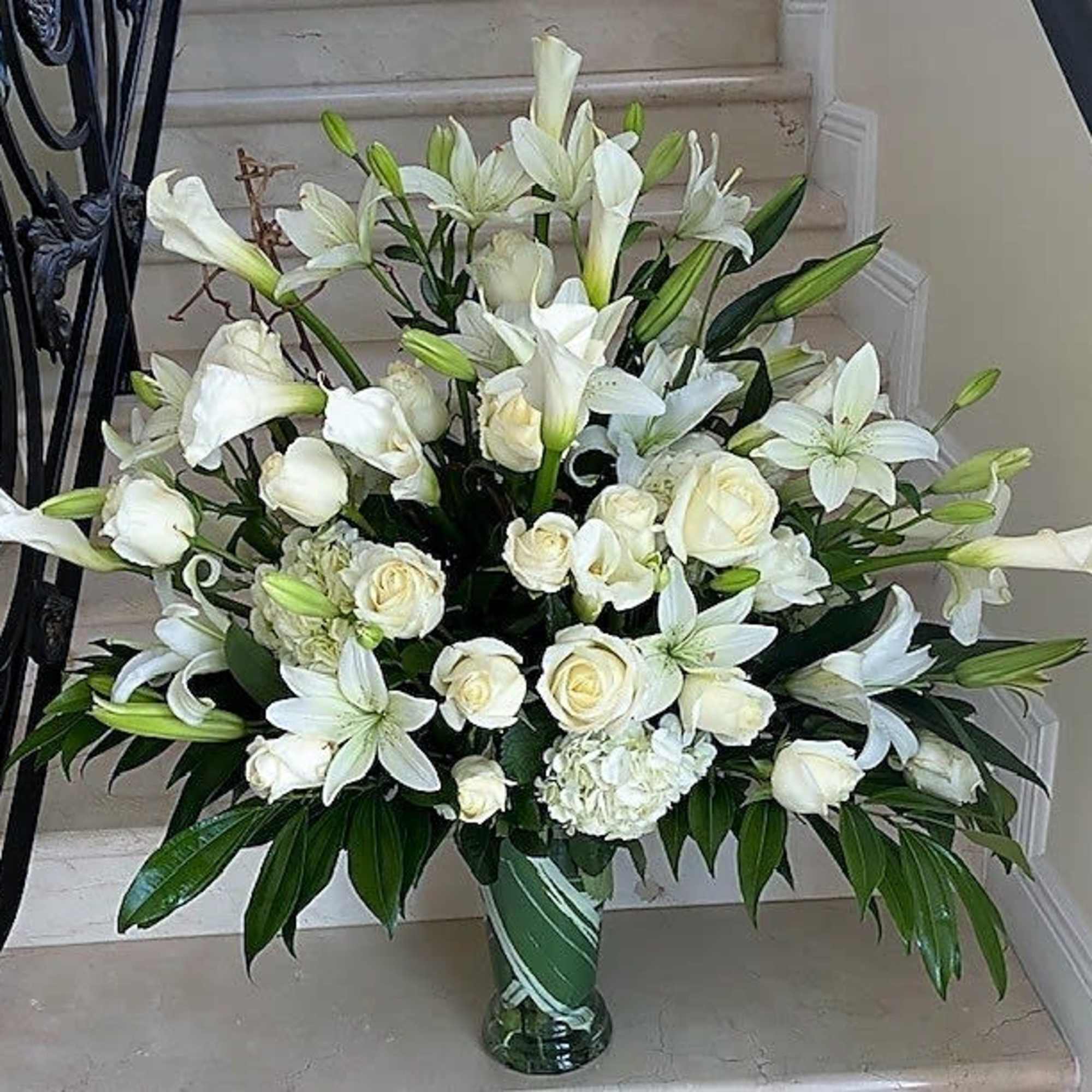 Tall white arrangement of roses, lilies, and calla lilies in a clear glass vase