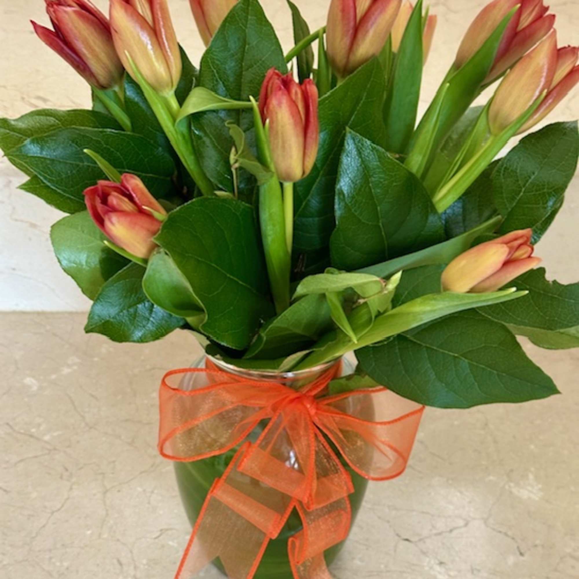 Bouquet of orange and peach tulips in a clear vase with an orange ribbon bow