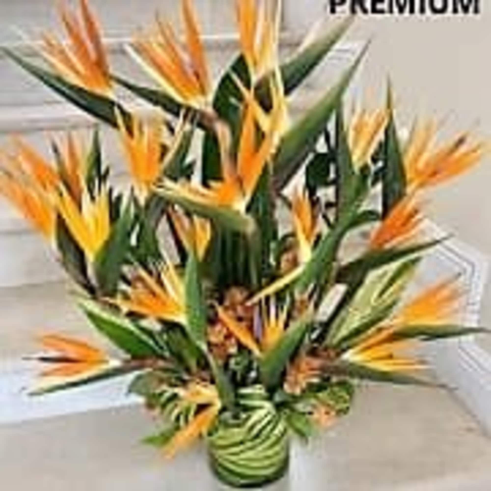 Tall tropical arrangement of orange and yellow flowers in a glass vase