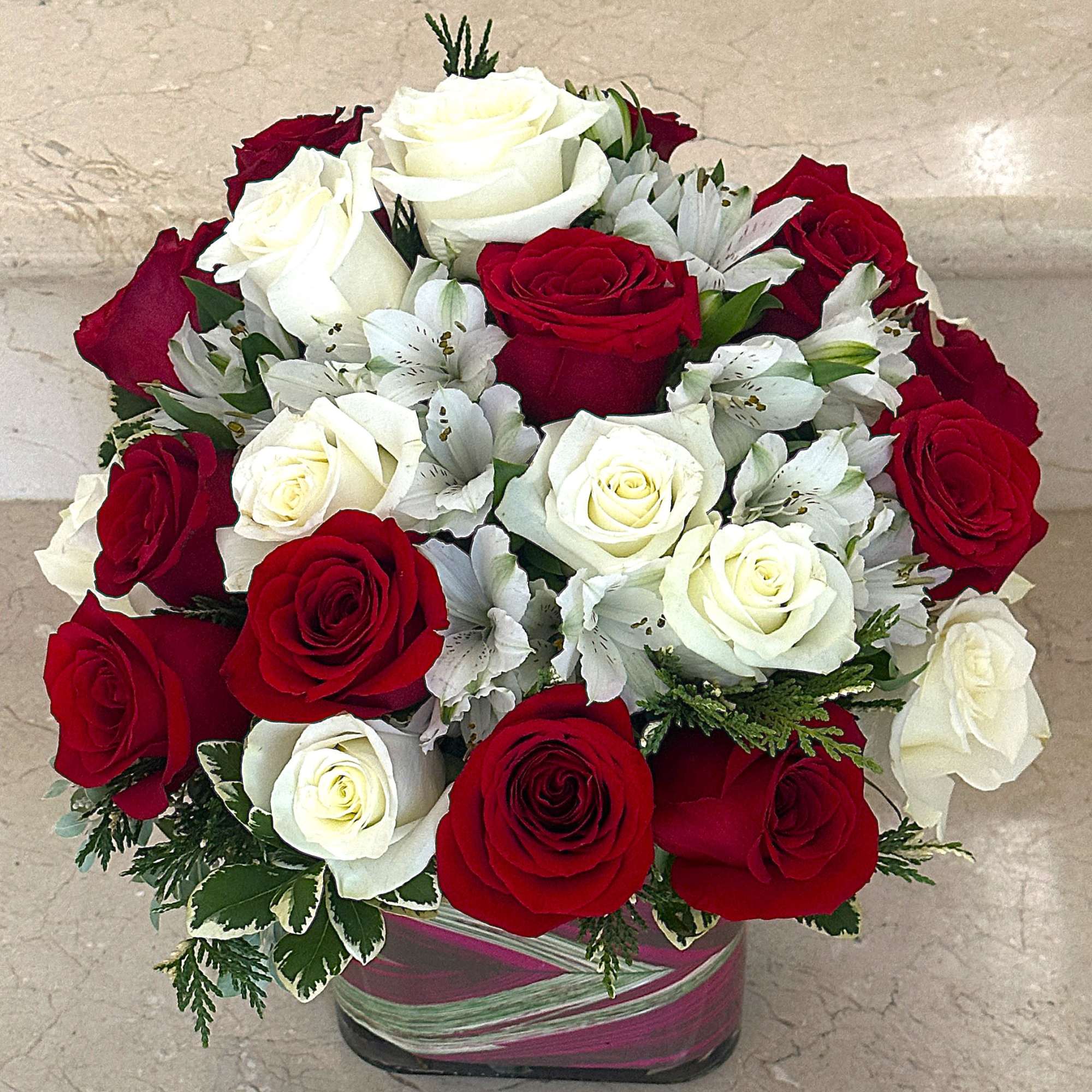 Compact arrangement of red and white roses with white alstroemeria in a ribbon-wrapped glass cube vase