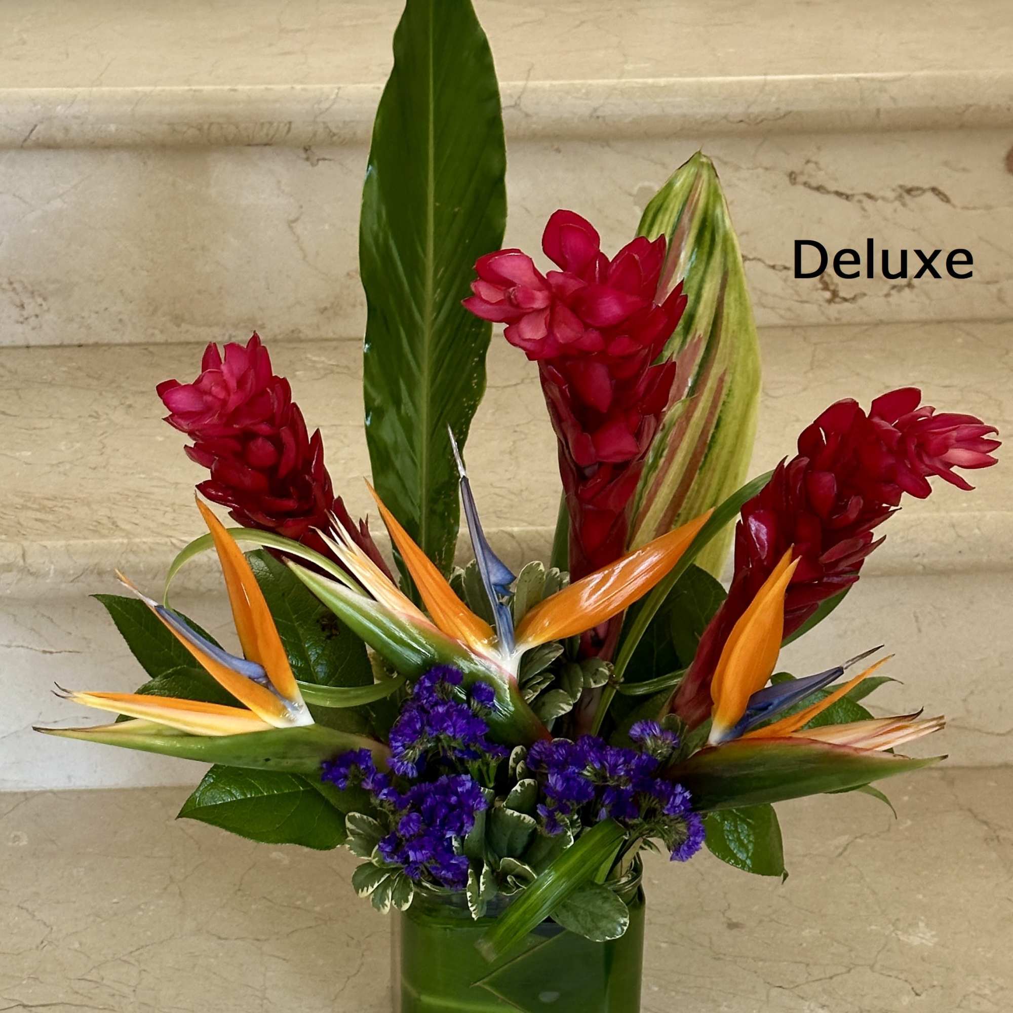 Tropical arrangement with red ginger, birds of paradise, and purple flowers in a green cube vase