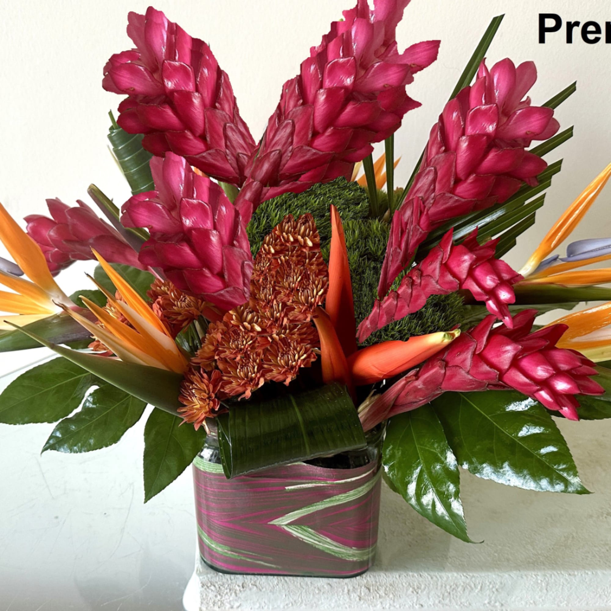 Tropical arrangement with pink ginger flowers and orange bird-of-paradise in a square vase