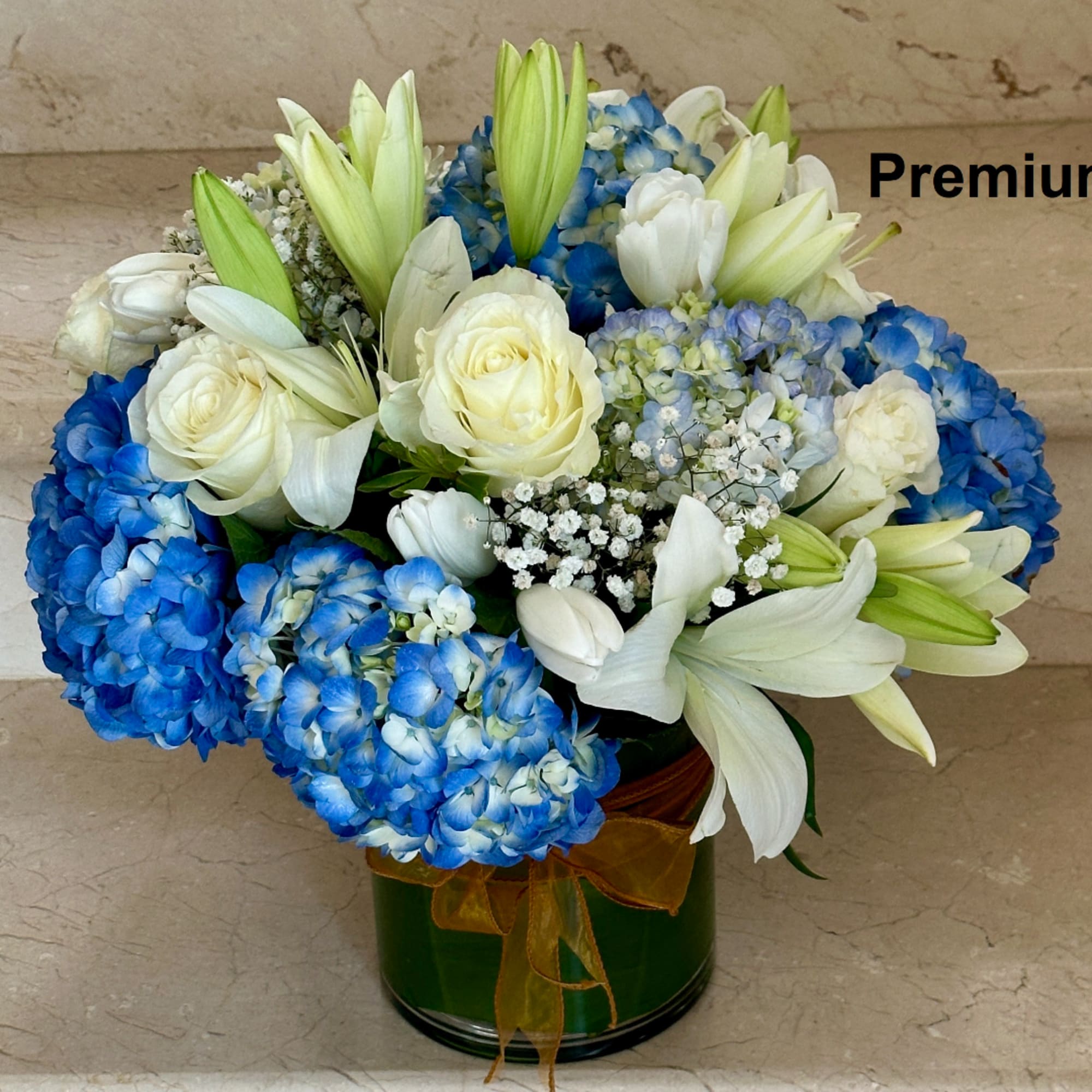 Blue hydrangeas, white roses, and lilies arranged in a green vase with ribbon.