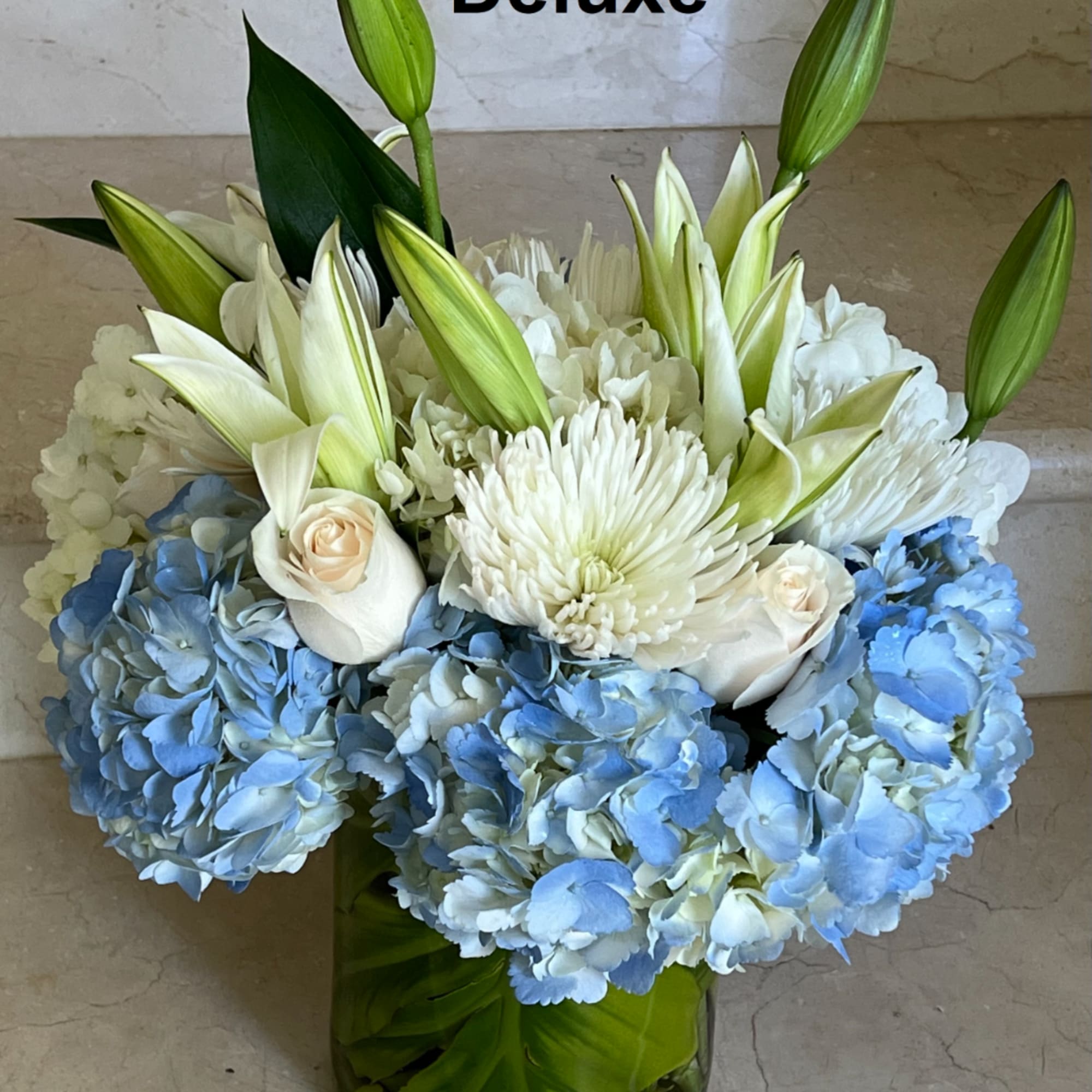 Blue hydrangeas and white lilies arranged in a glass vase