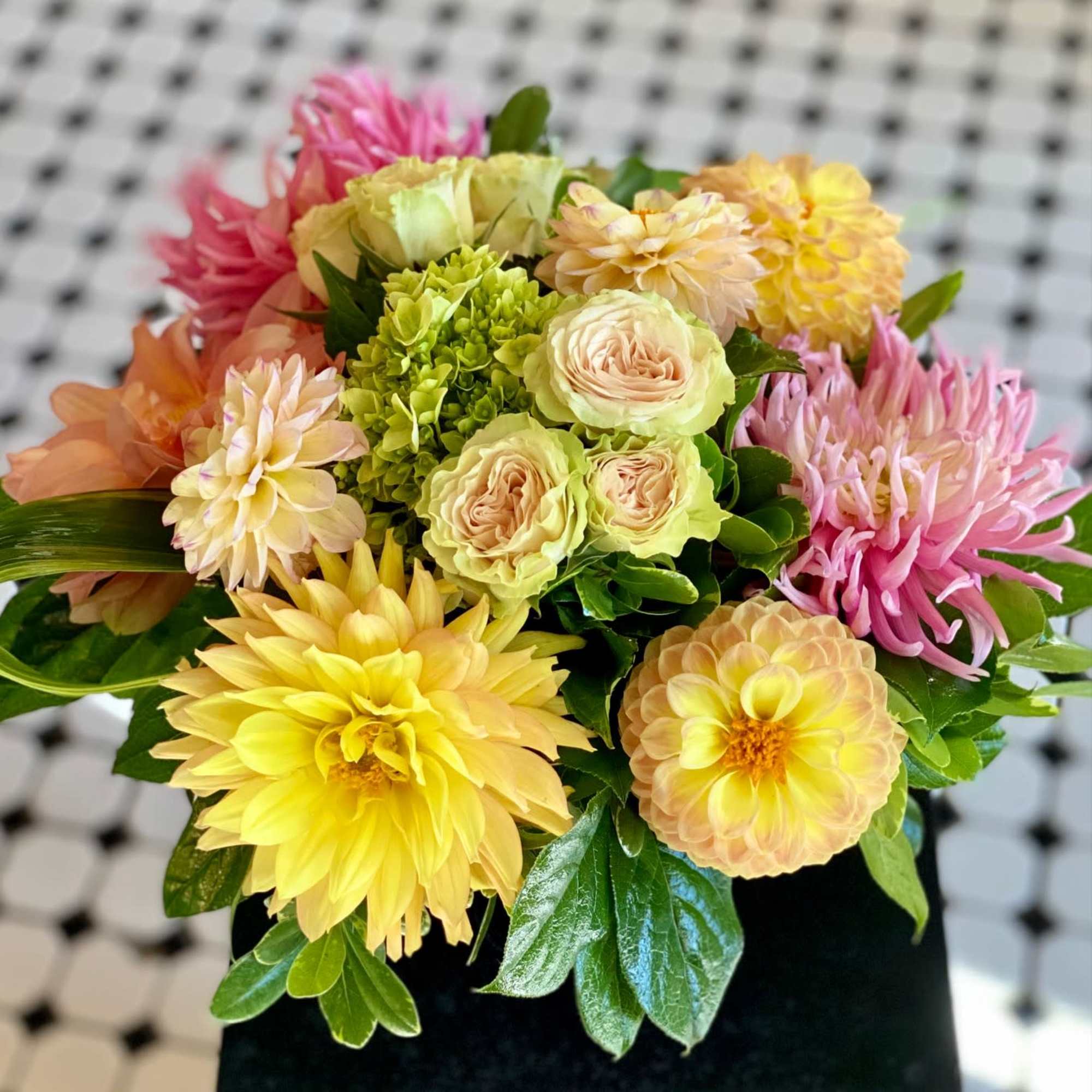 Mixed bouquet of yellow, pink, and peach flowers in a black container