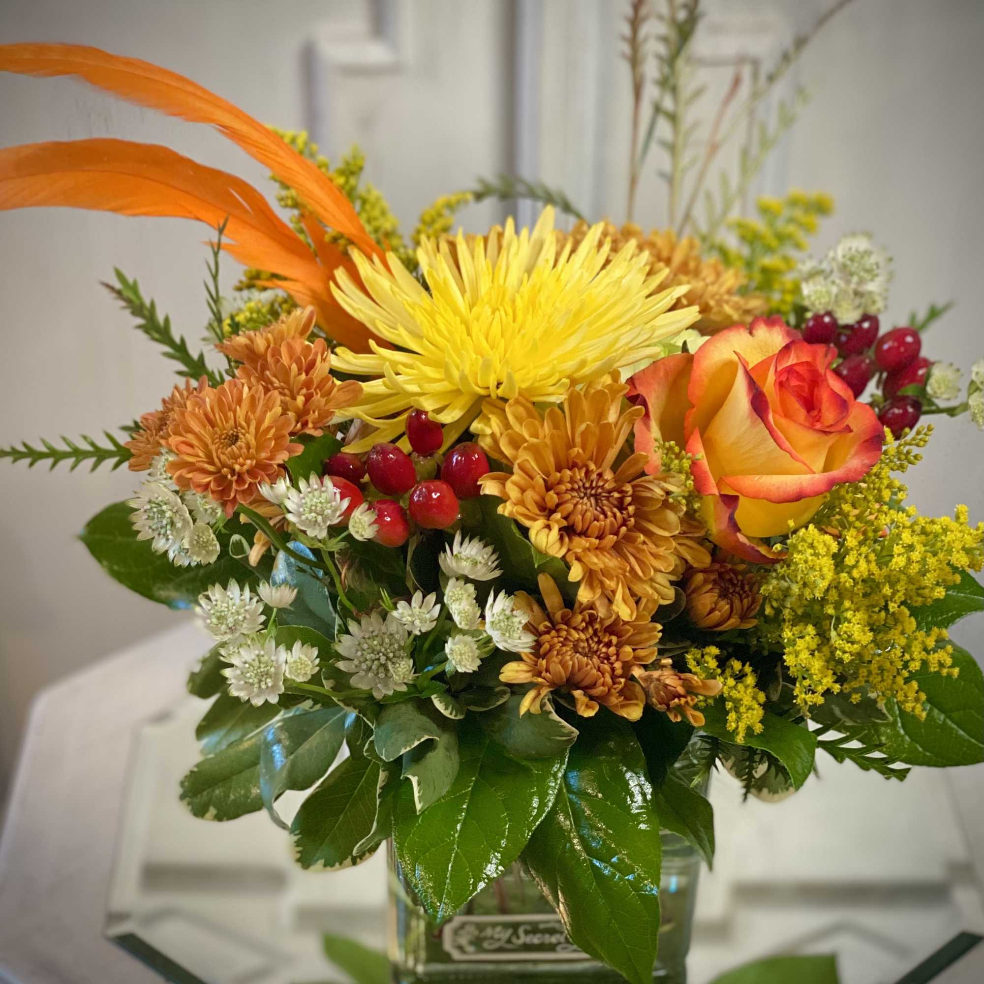 Orange and yellow floral arrangement in a glass vase with a rose and chrysanthemums