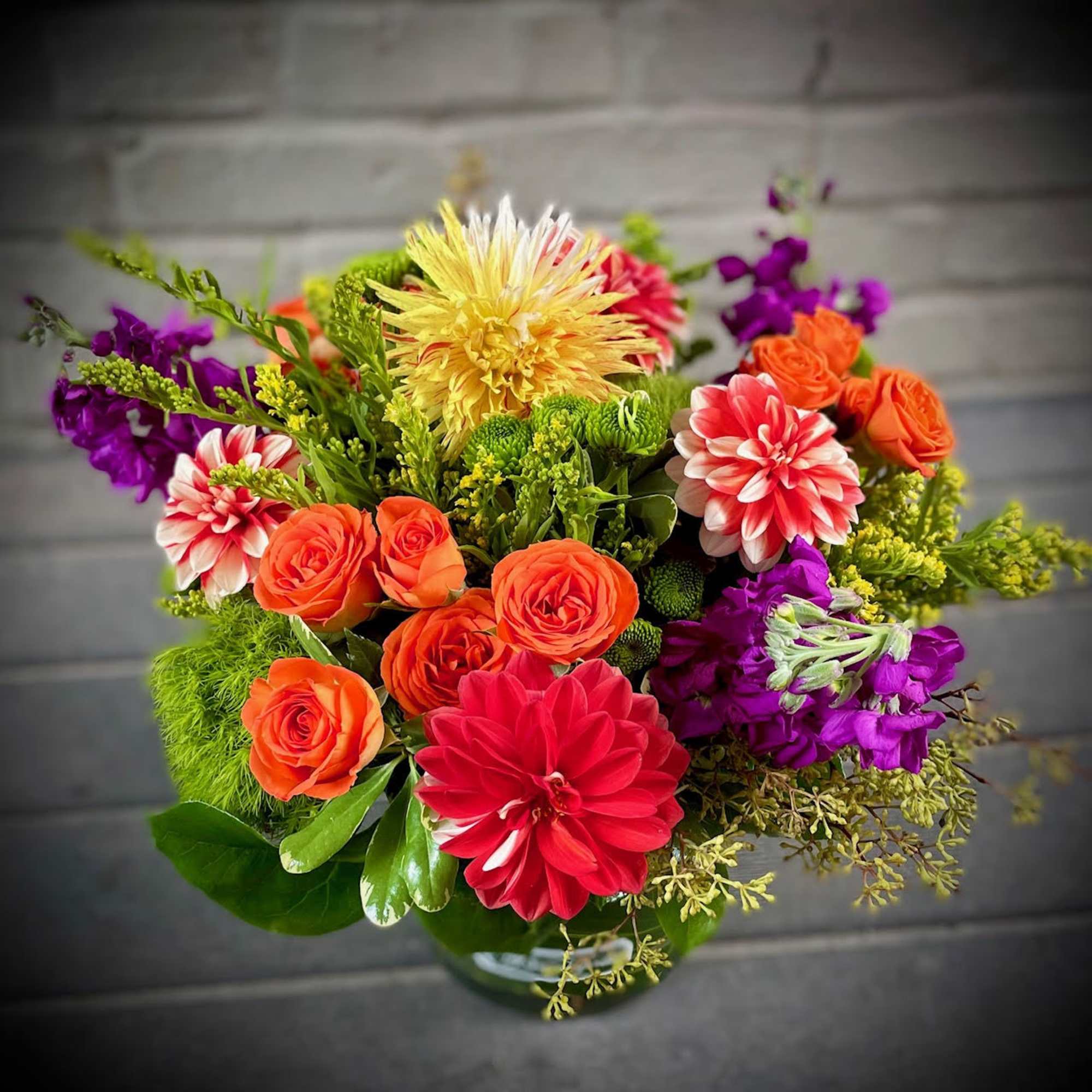 Colorful mixed bouquet with orange roses, dahlias, and purple blooms in a vase