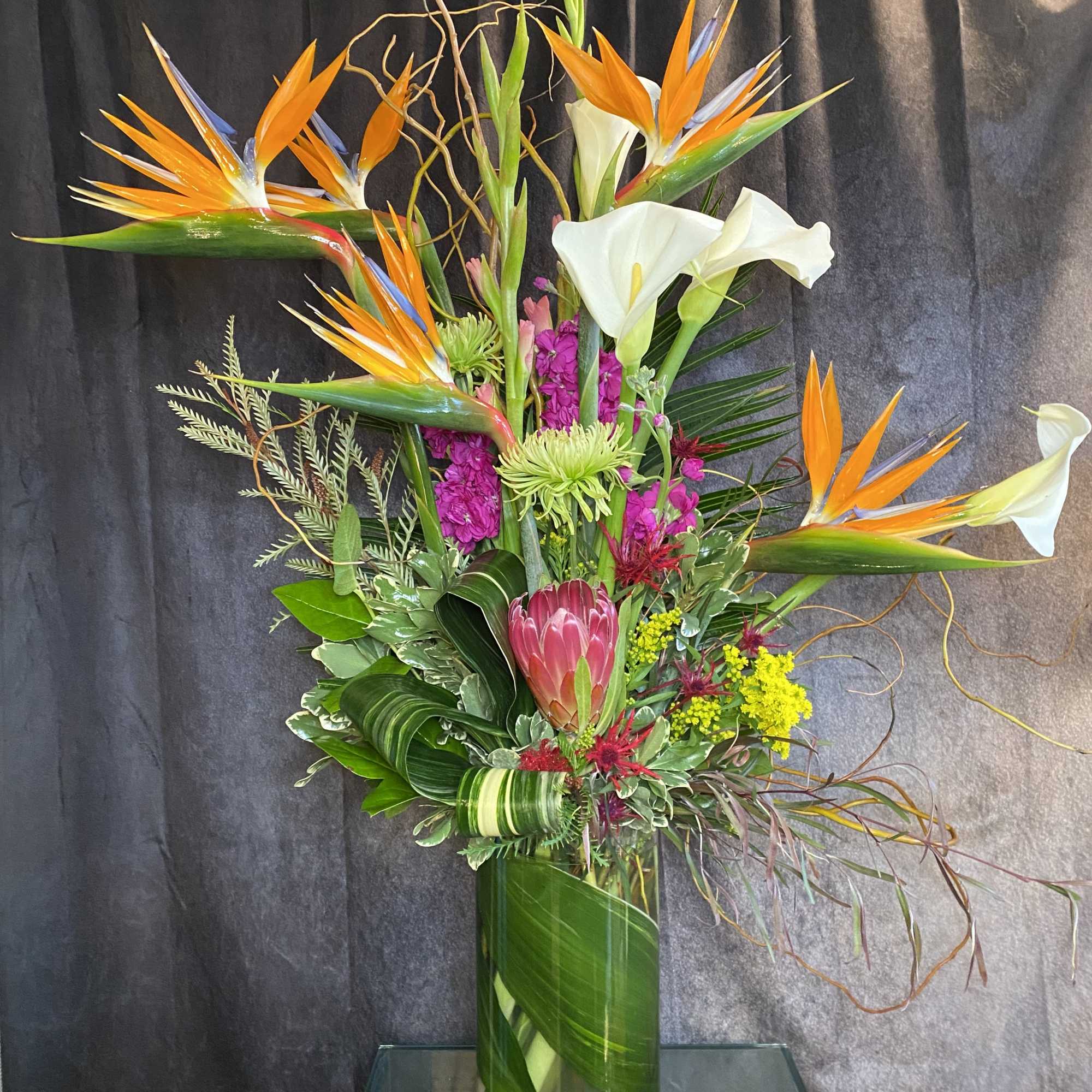 Tall tropical arrangement with bird of paradise and white calla lilies in a glass vase
