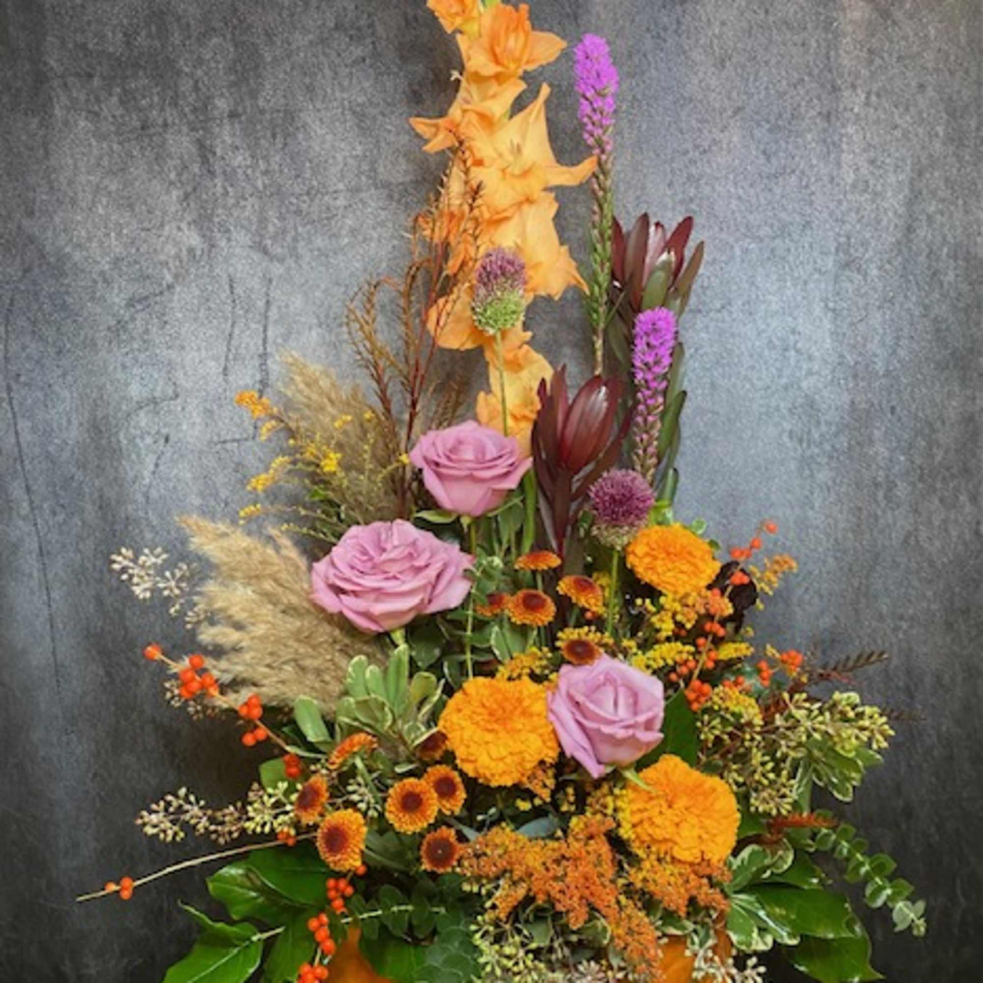 Tall mixed floral arrangement in an orange pumpkin-shaped container