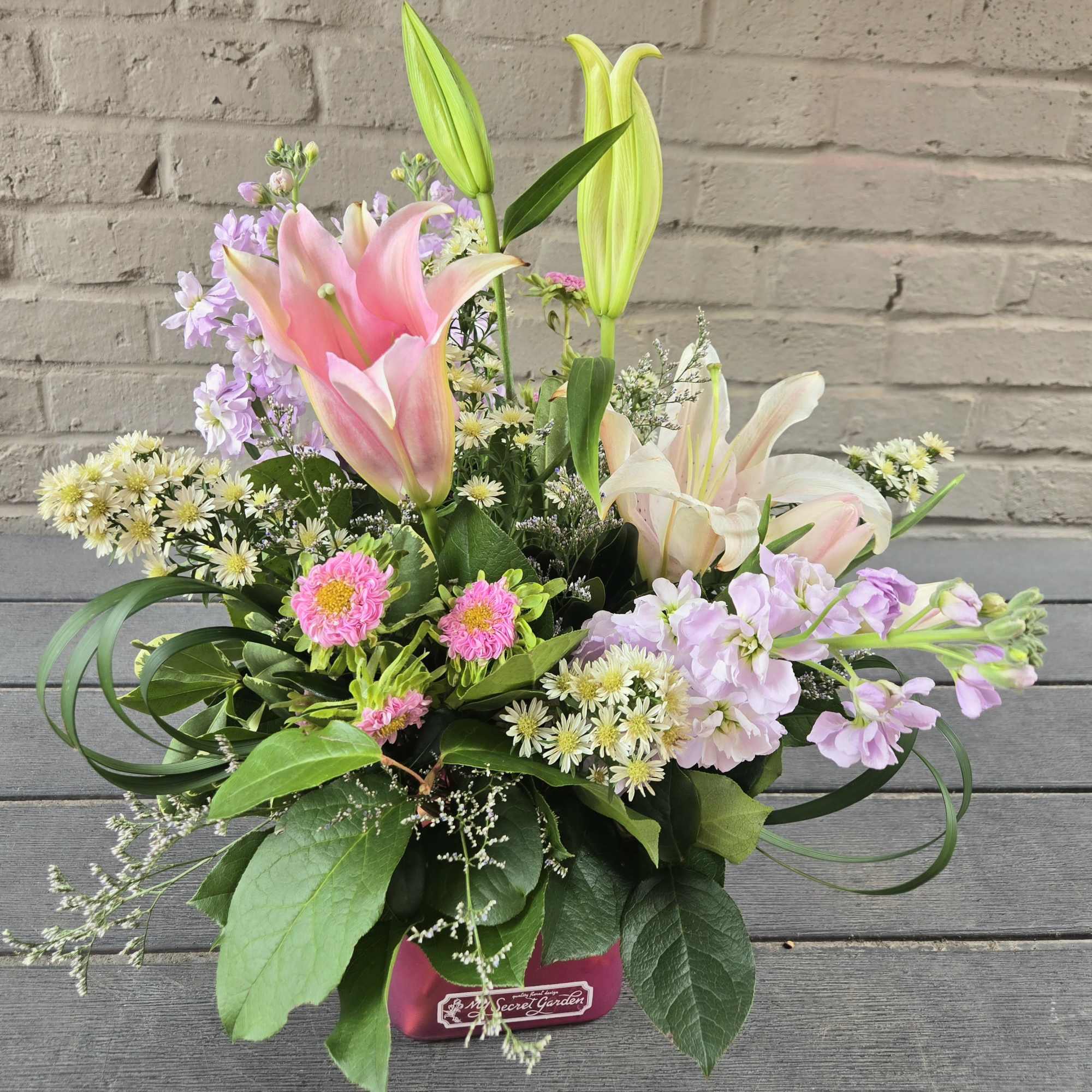Pink and white lilies with lavender flowers in a pink container