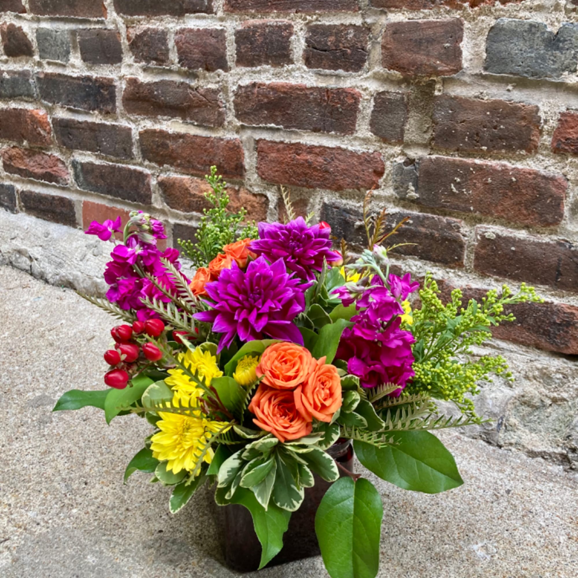 Colorful mixed bouquet in a dark container with orange, purple, and yellow flowers