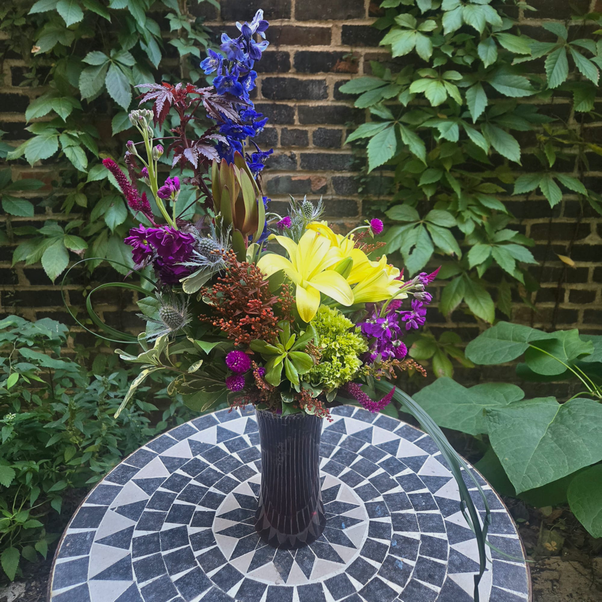 Colorful mixed flower arrangement in a dark vase on an outdoor table